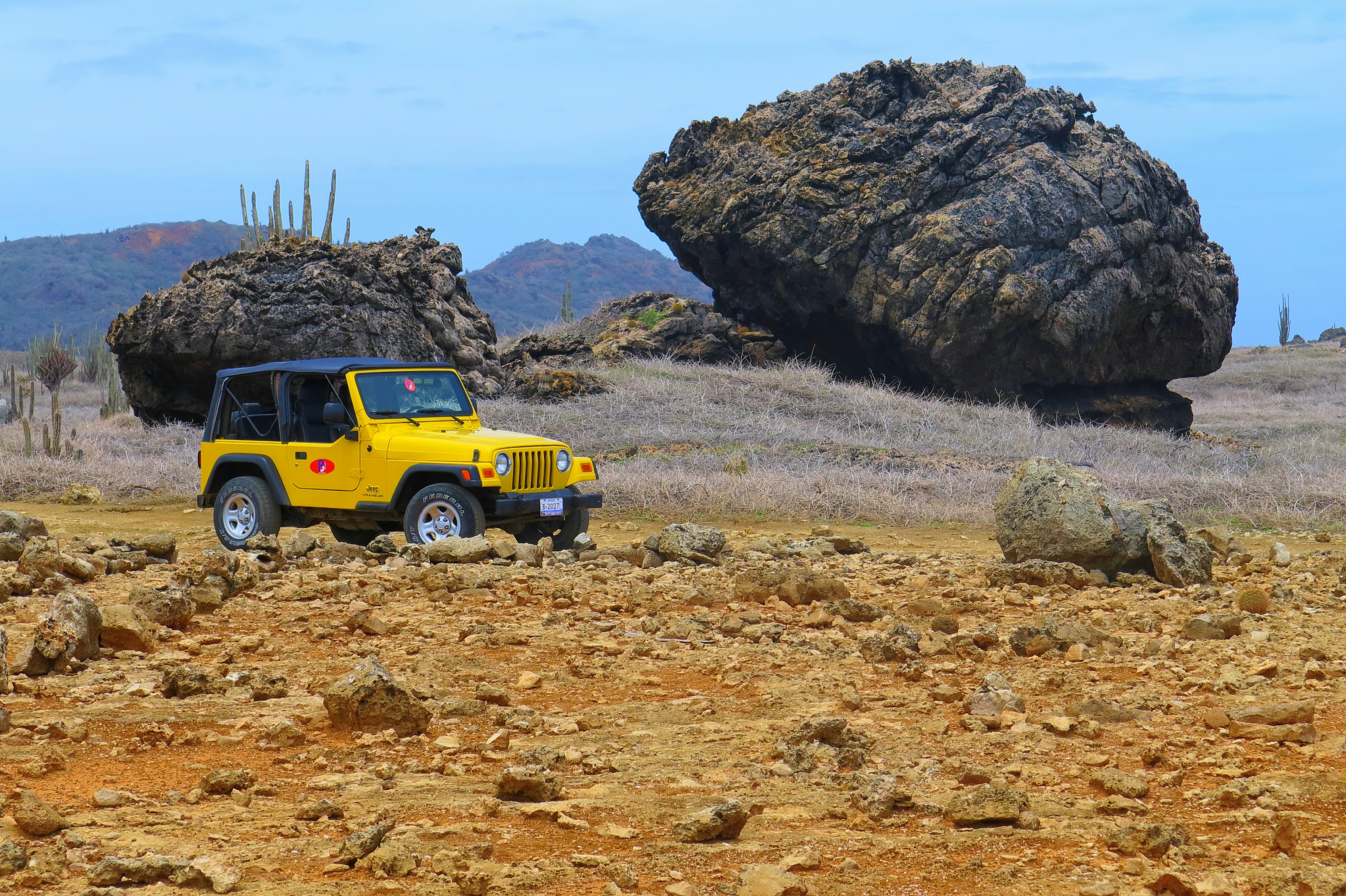 A yellow Jeep drives by huge boulders in a rocky landscape