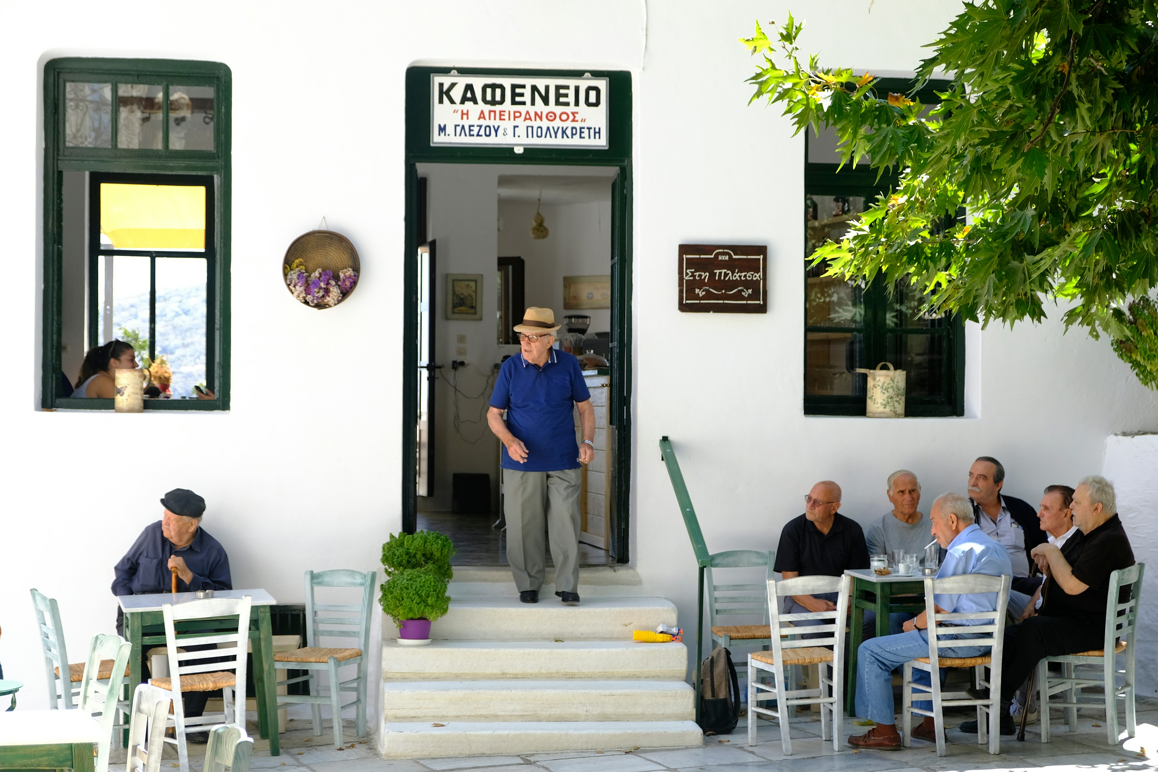 One man walks out the door while other men sit at tables outside a traditional coffee shop in Apiranthos village in Naxos island, Greece.