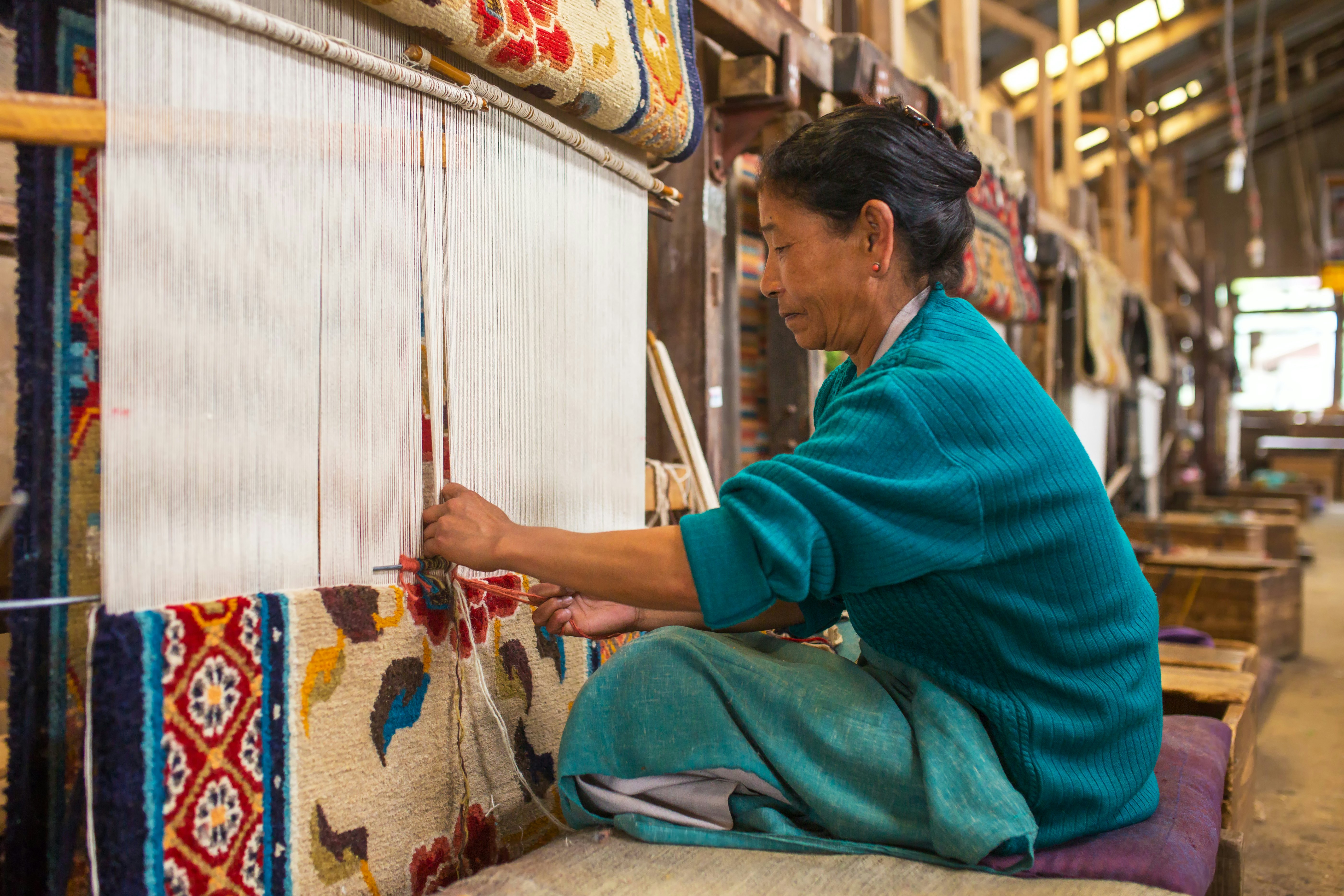 A woman weaves a carpet at a loom in a workshop