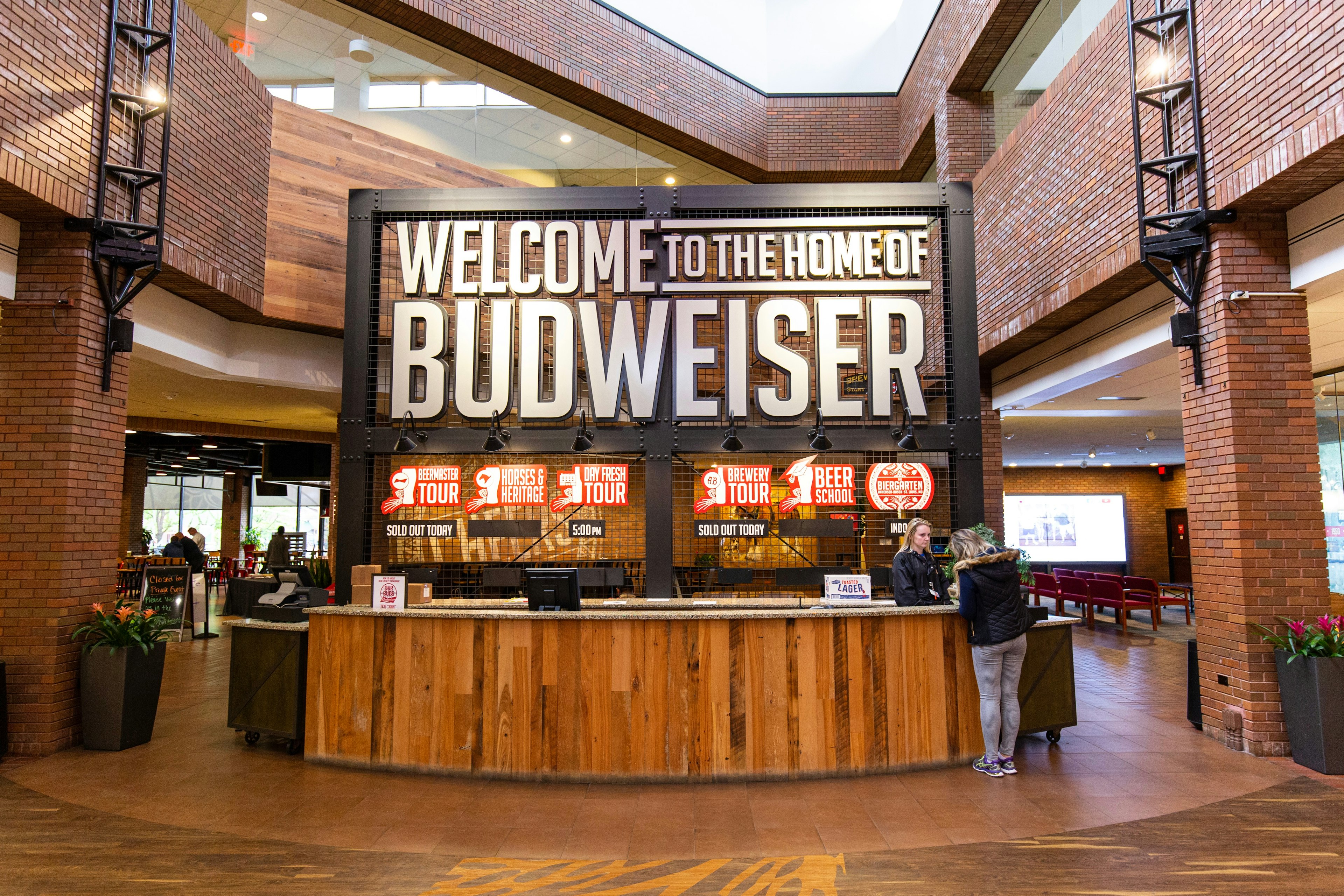 The welcome desk at a beer factory with a large sign that reads "Welcome to the home of Budweiser"