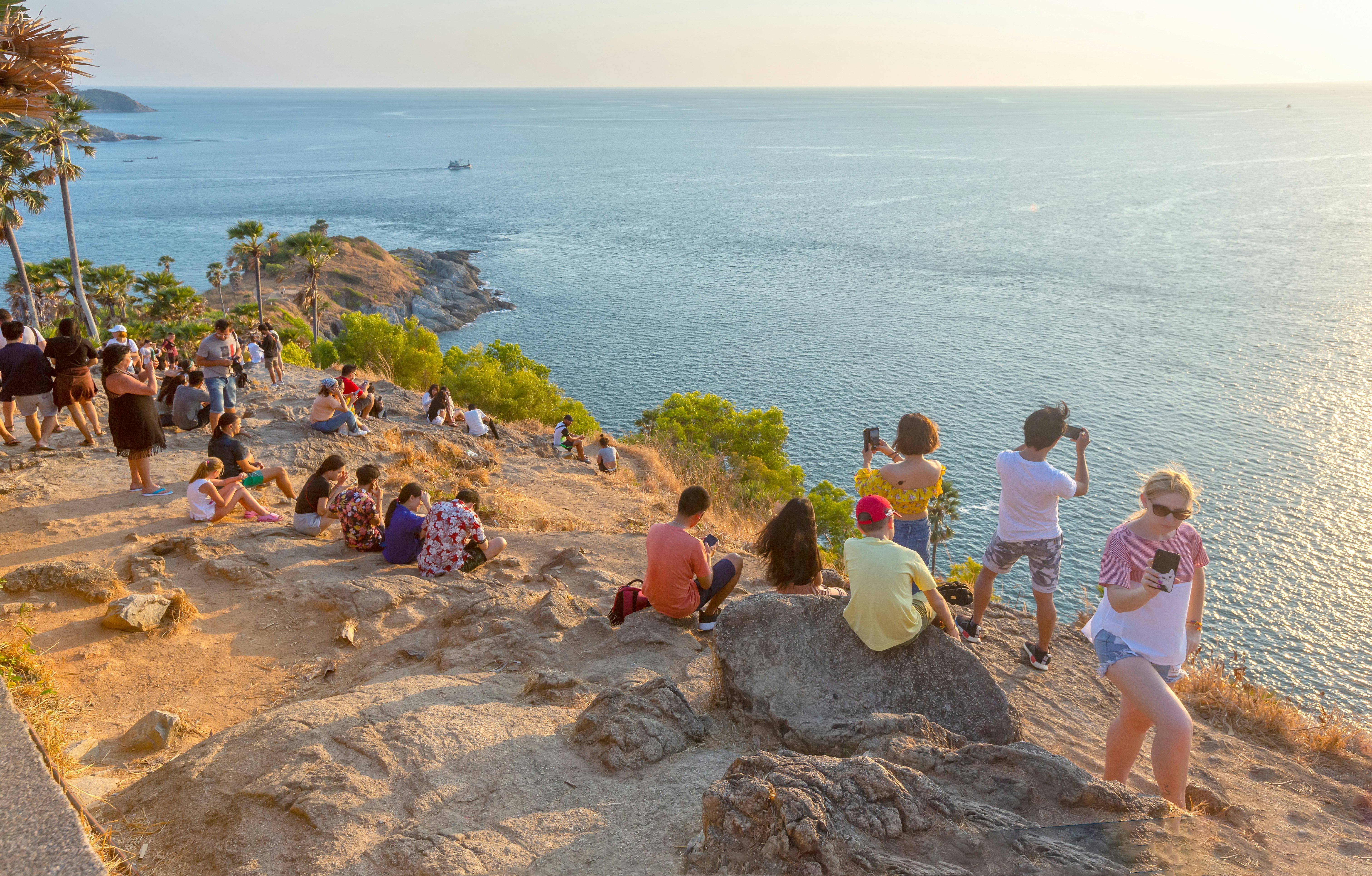 People gather on a rocky coastline to watch the sunset over the sea