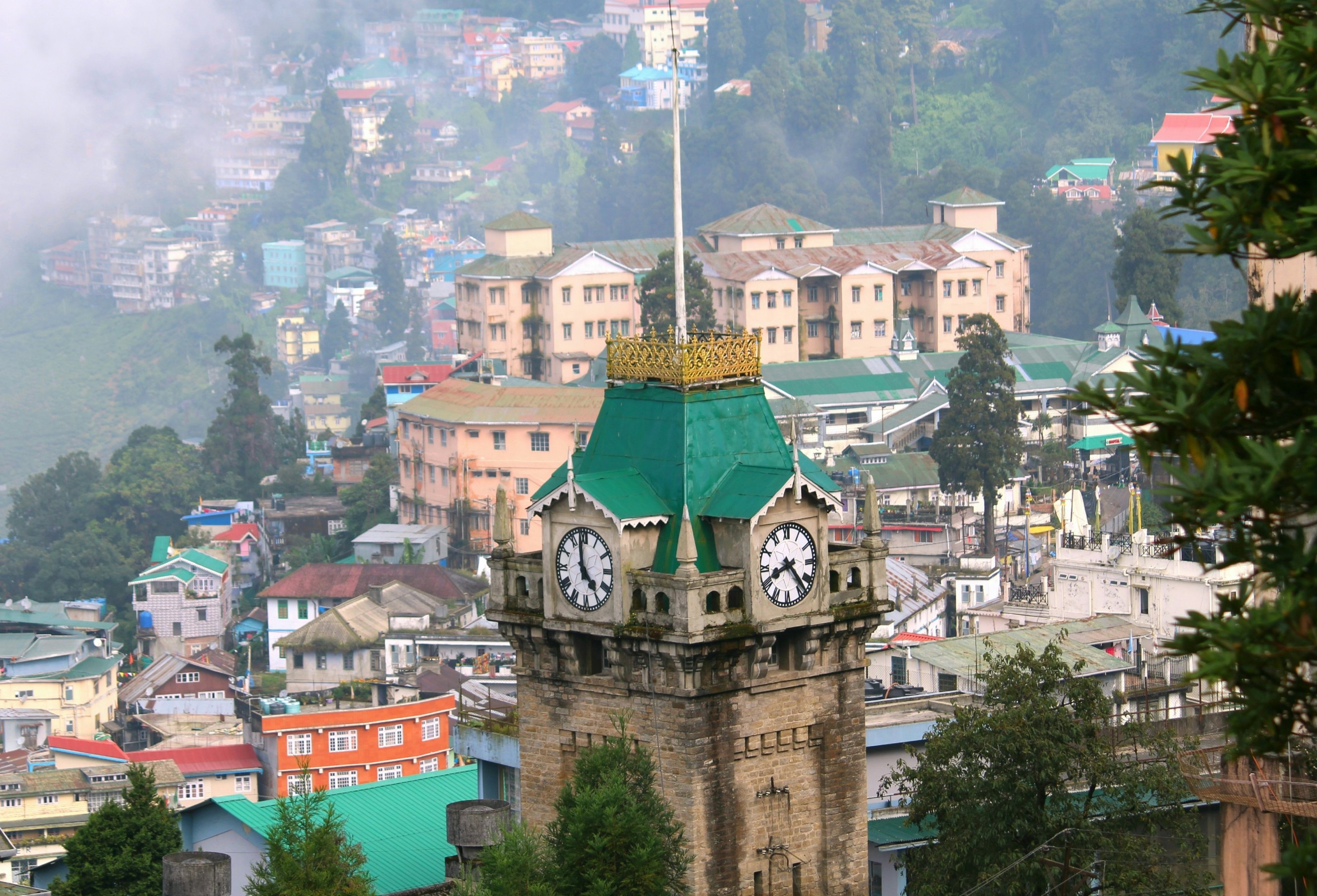 A stone clock tower in a hilly town with two clock faces showing different times