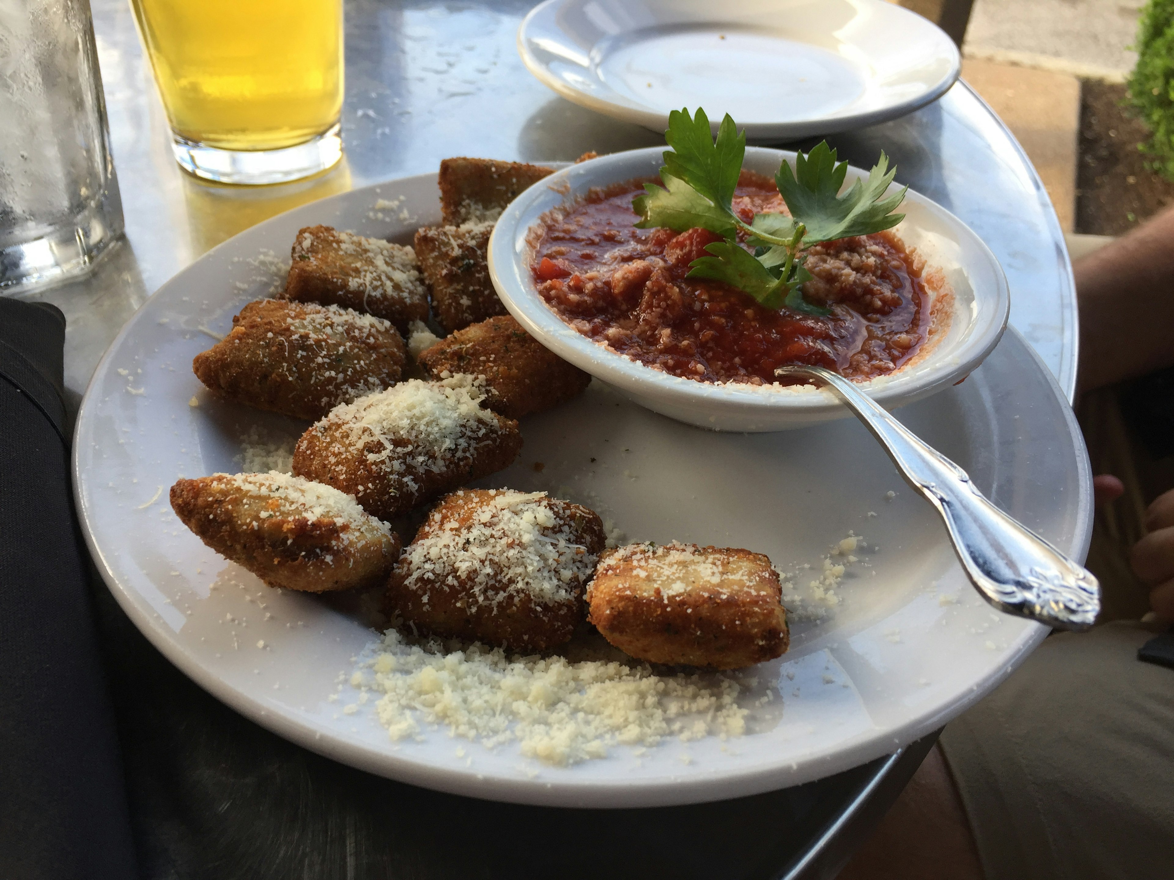 Toasted ravioli sprinkled with parmesan cheese with marinara sauce garnished with parsley on a white plate