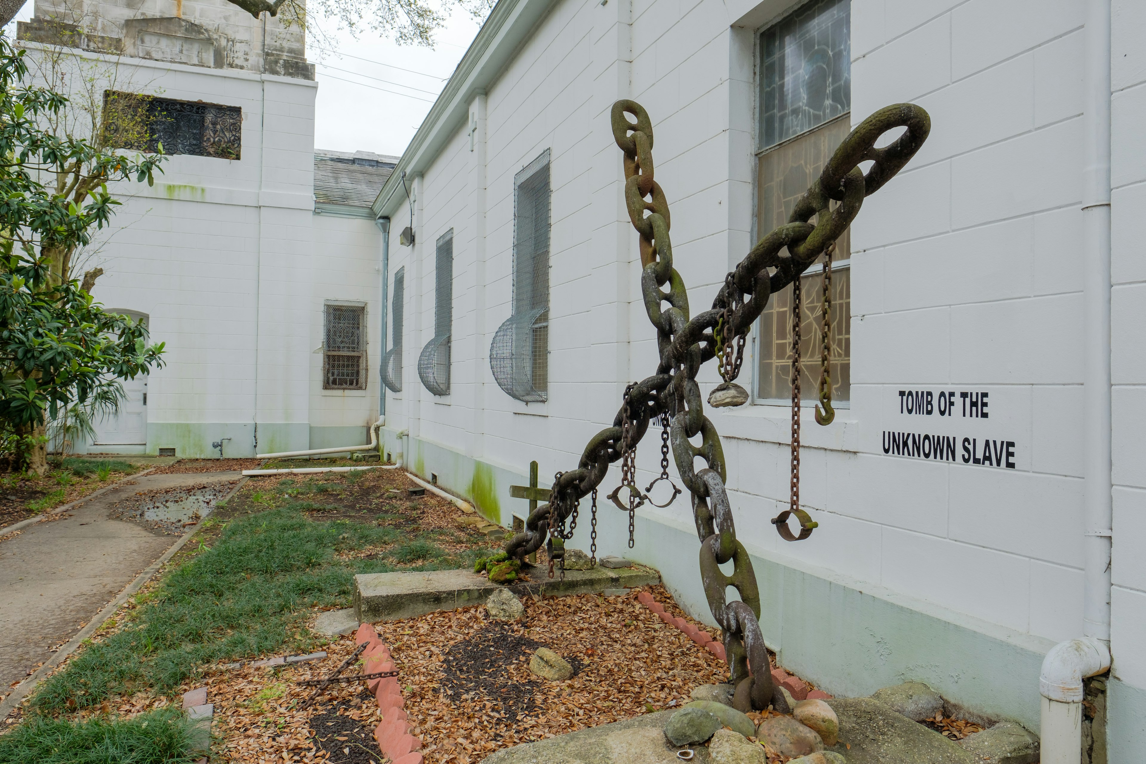 A cross made of chain links stands in the yard of a white-painted church