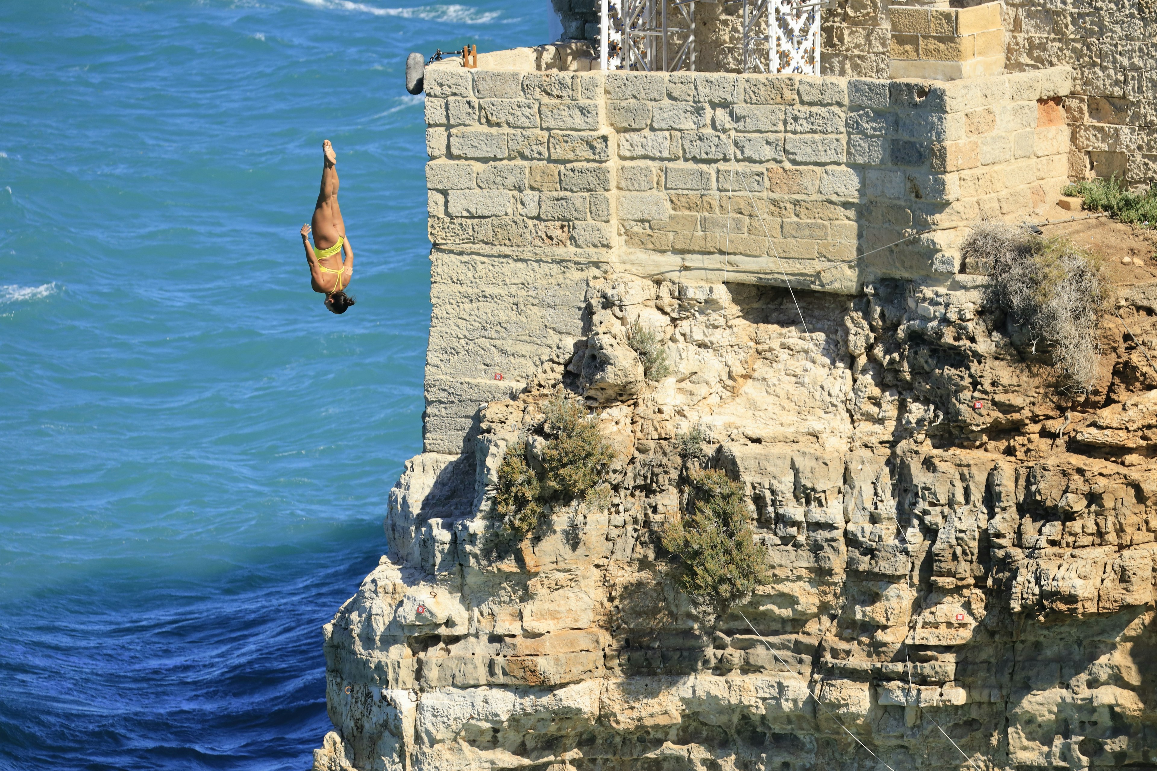 A professional cliff diver plunging straight down head first beside a sheer rock face