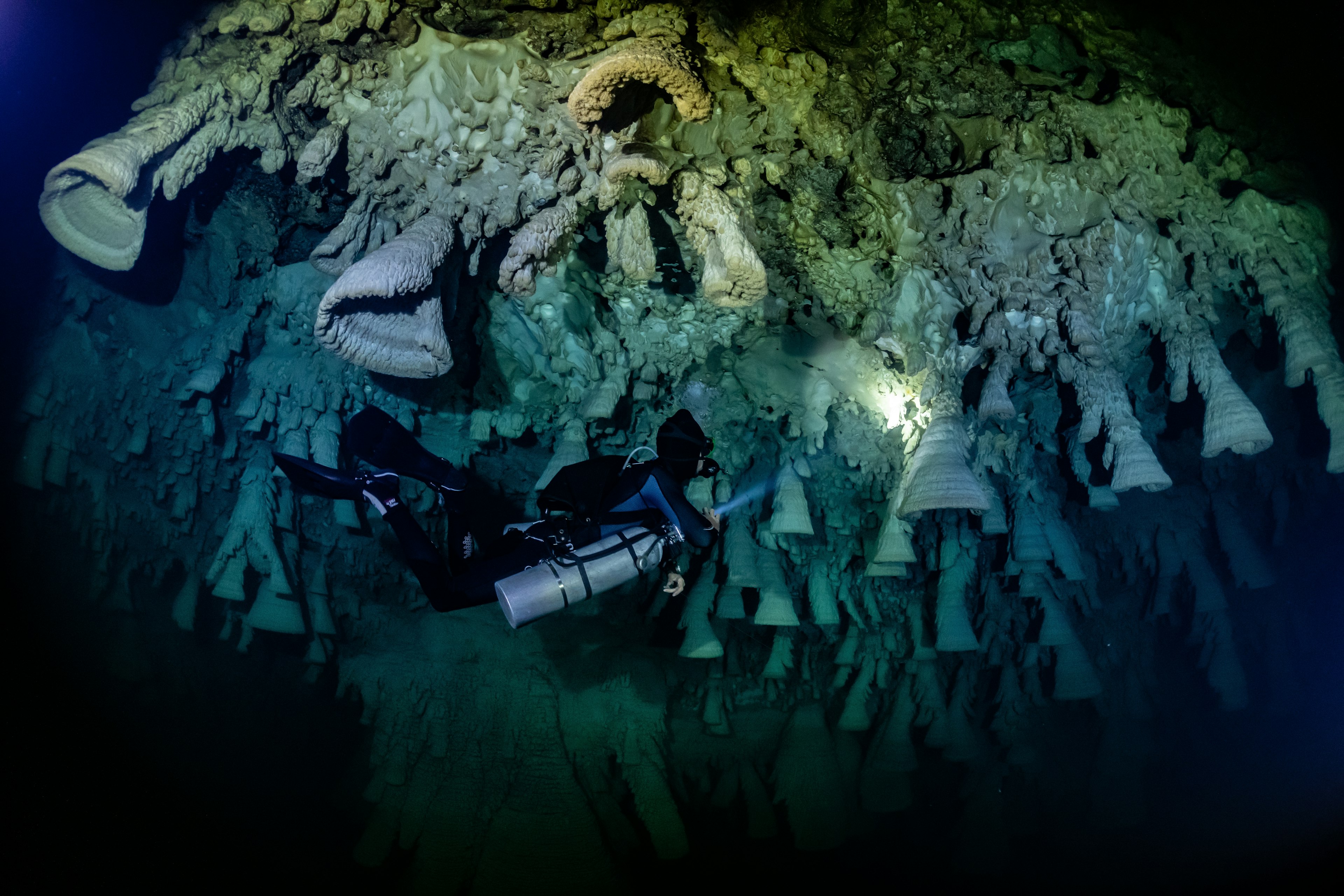 A scuba diver shines a beam on cone-like underwater carbonate formations known as Hells Bells