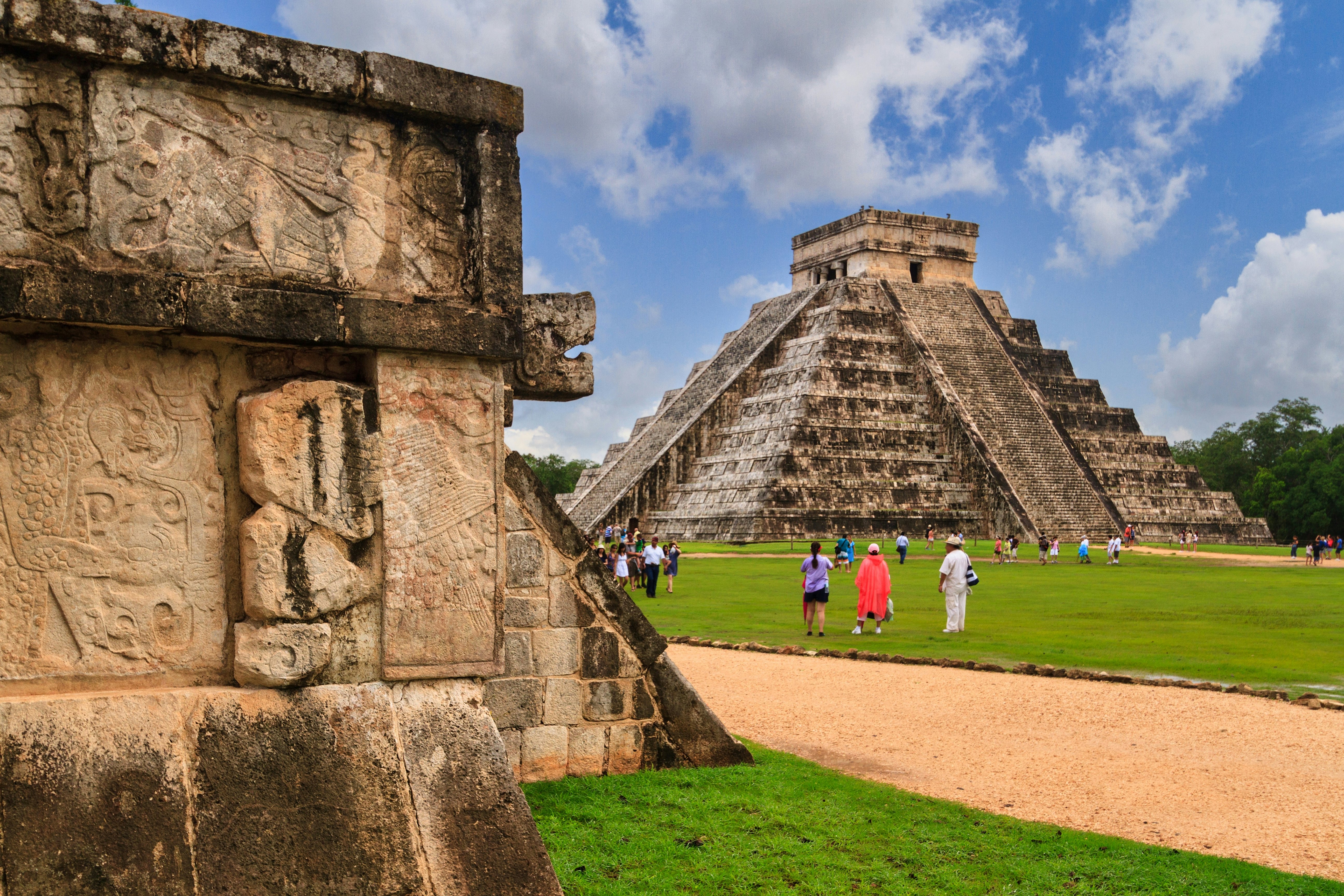 Tourists mill around ancient stone pyramids with large stepped sides