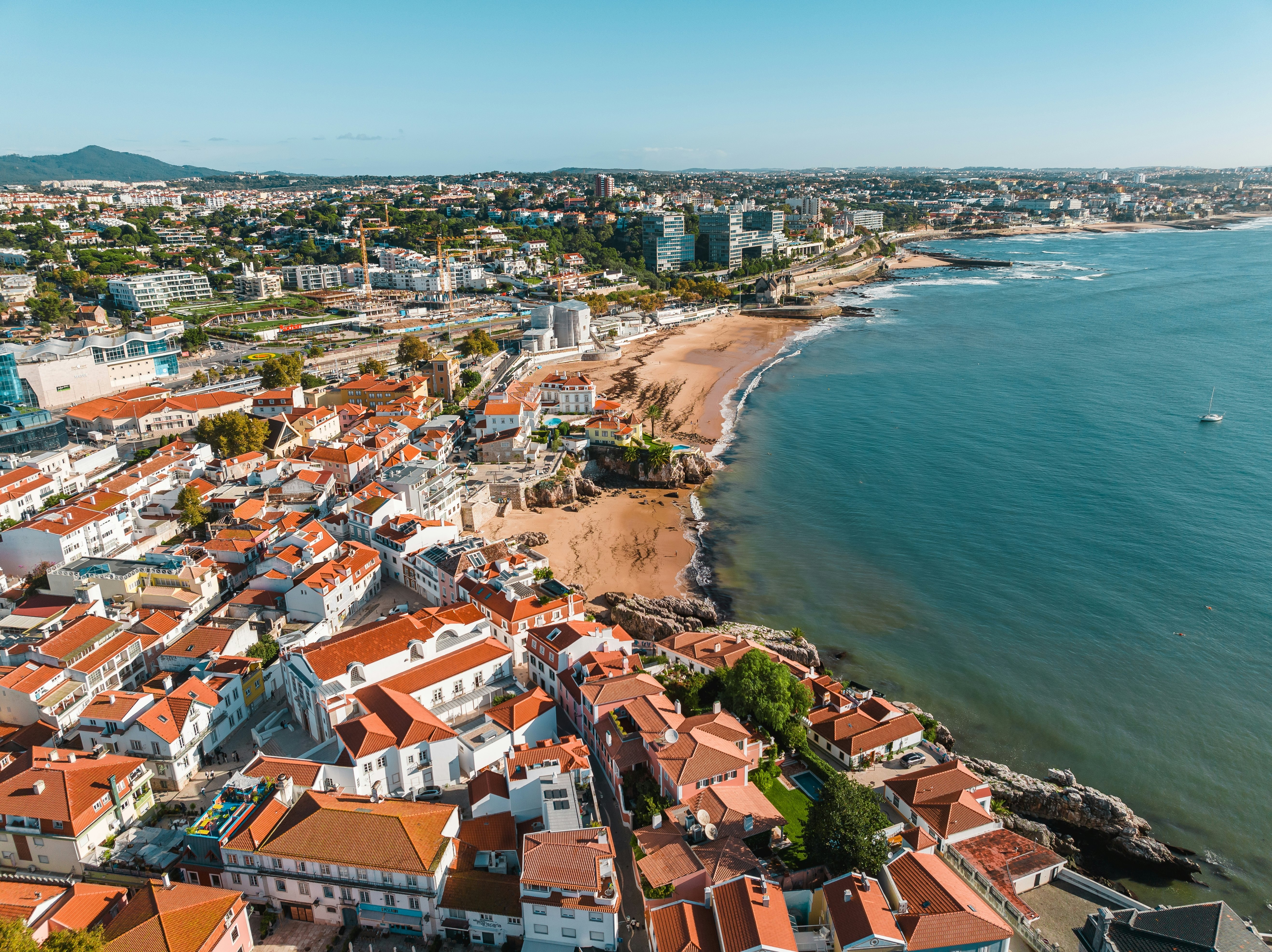 An aerial view of a seafront town with red-roofed buildings and large stretches of beach