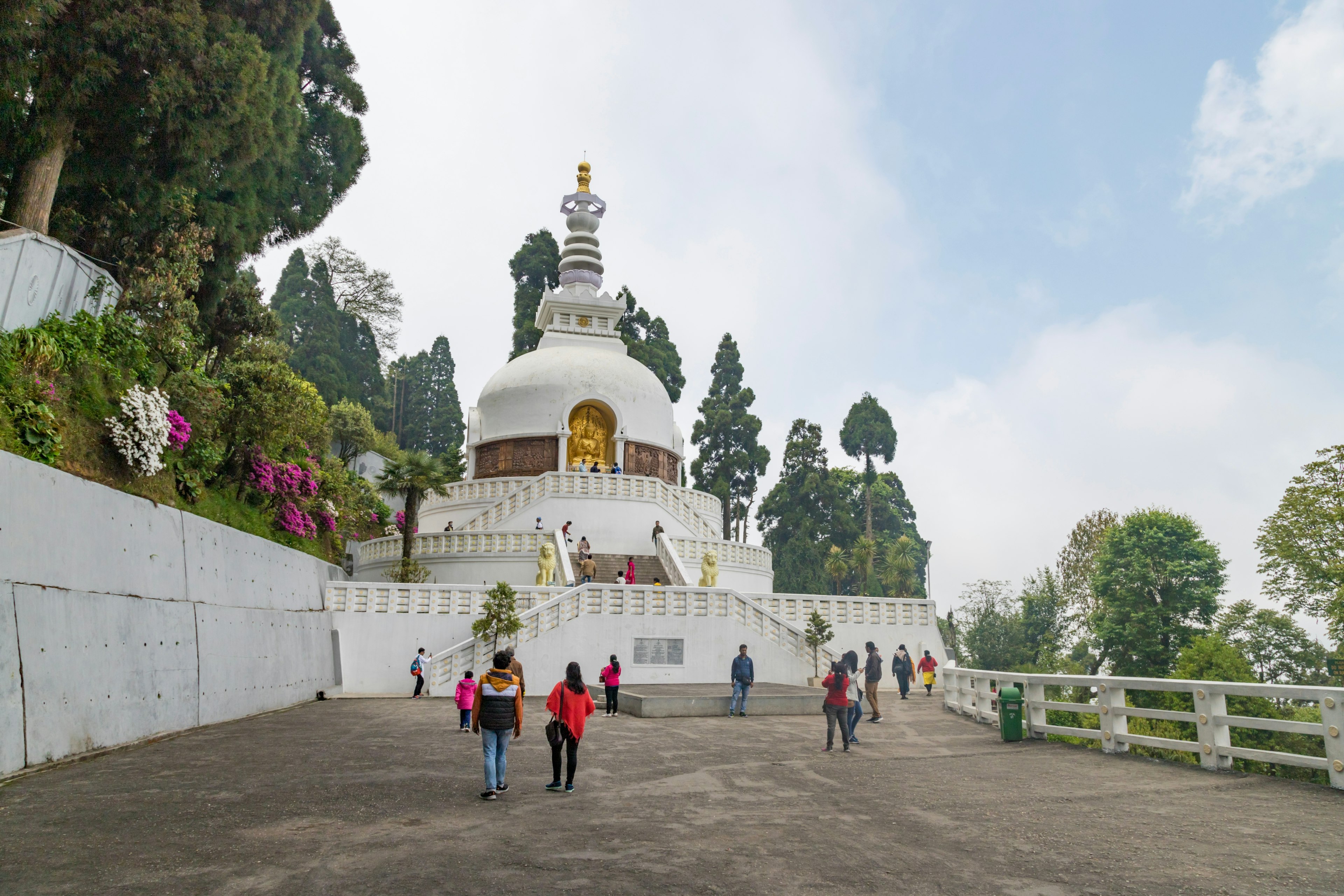 People walk towards a large white domed pagoda at the top of a set of stairs