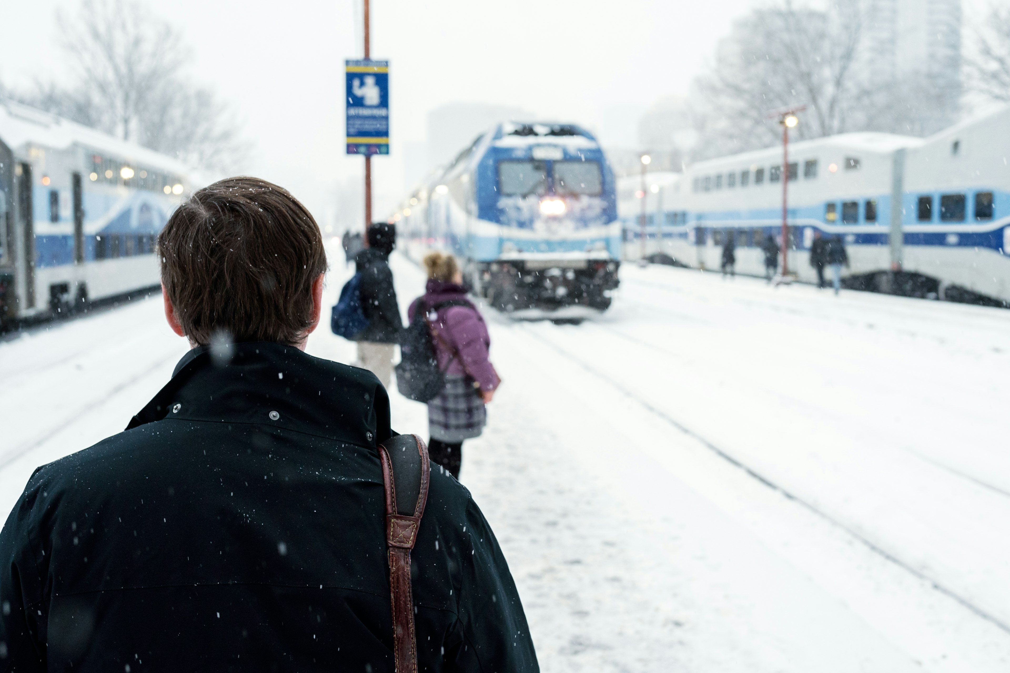 A group of commuters wait in the snow for the arrival of an Exo train at Lucien L’Allier station, Montréal, Québec, Canada