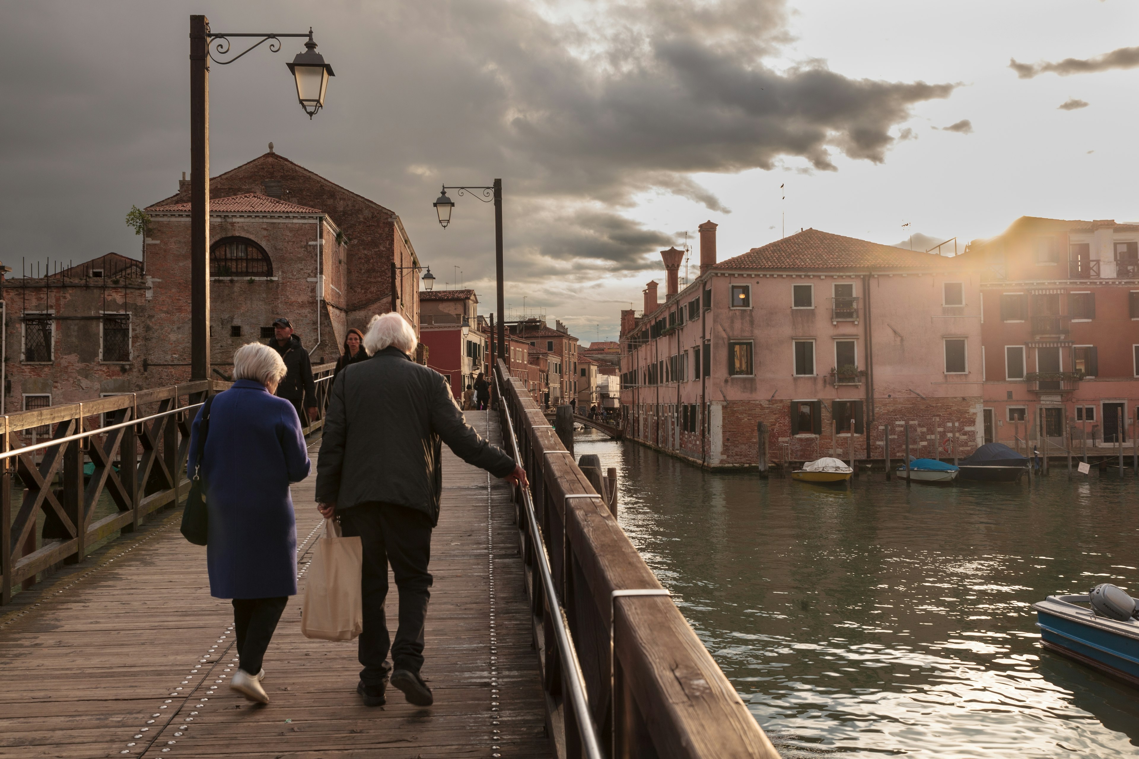 An elderly couple walks at sunset on a bridge in Venice, Veneto, Italy