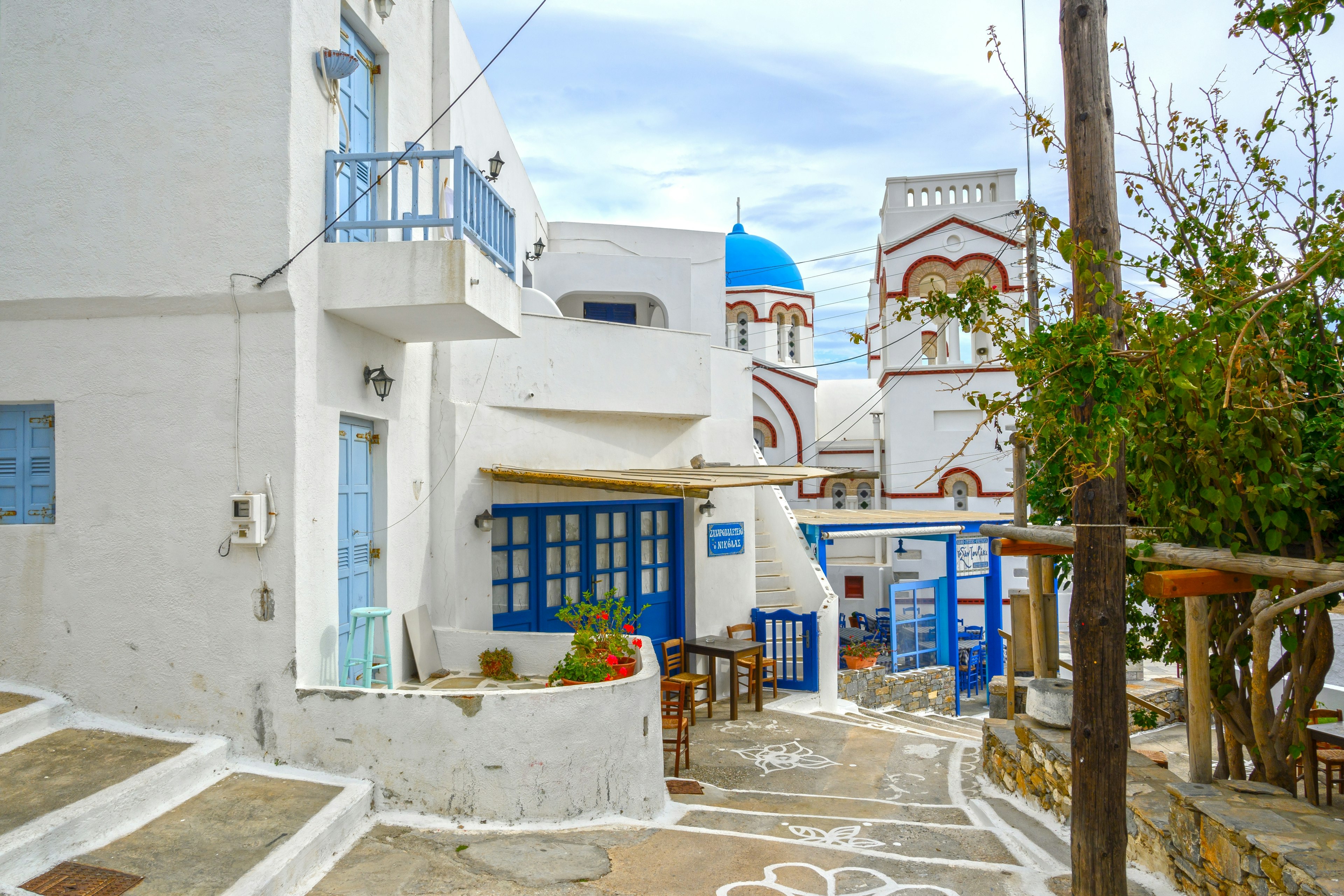 A street scene of Tholaria village with narrow streets and traditional Cycladic architecture, blue-trimmed white buildings.