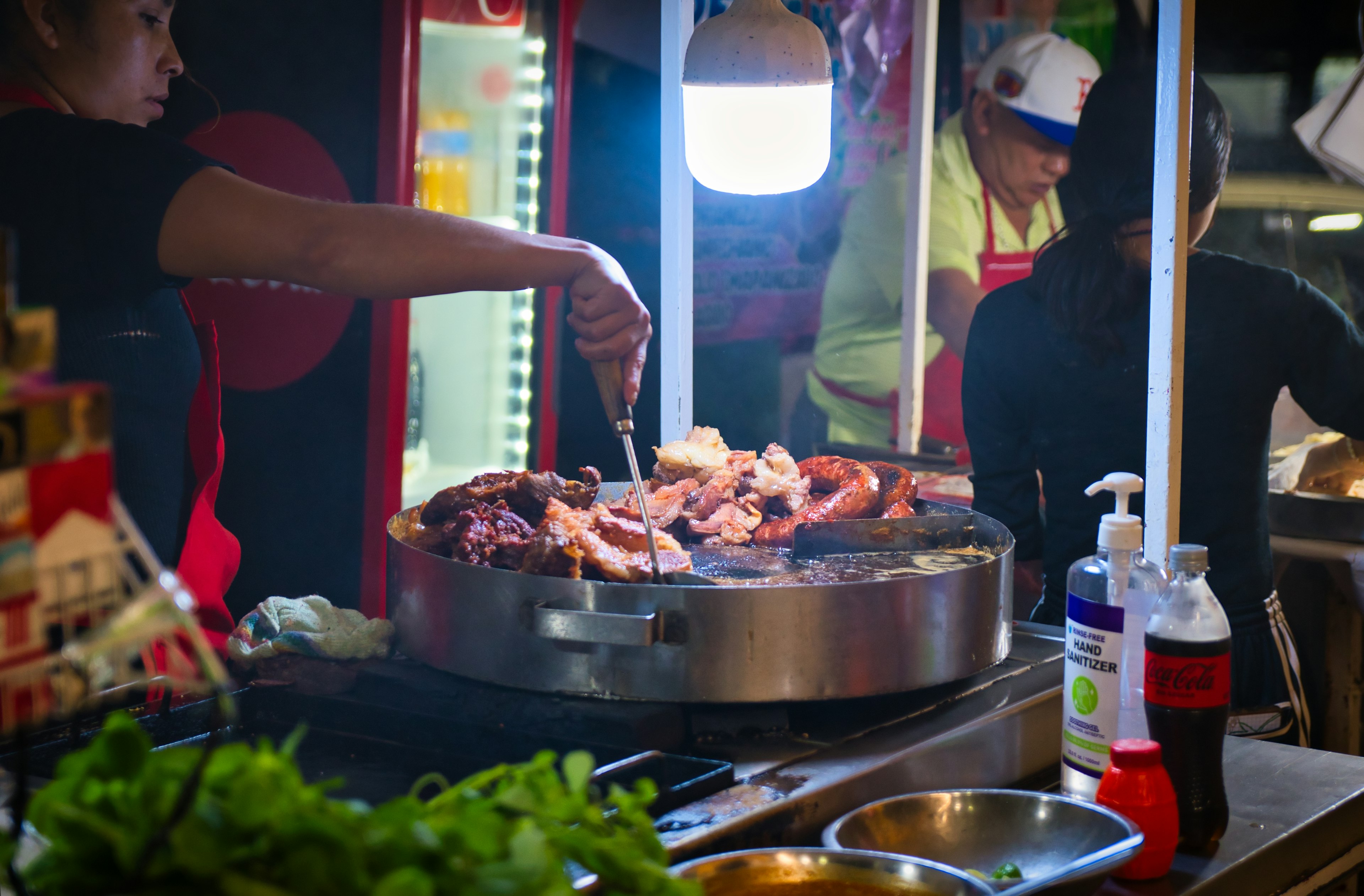 A food vendor prepares meat for tacos at a stall at night