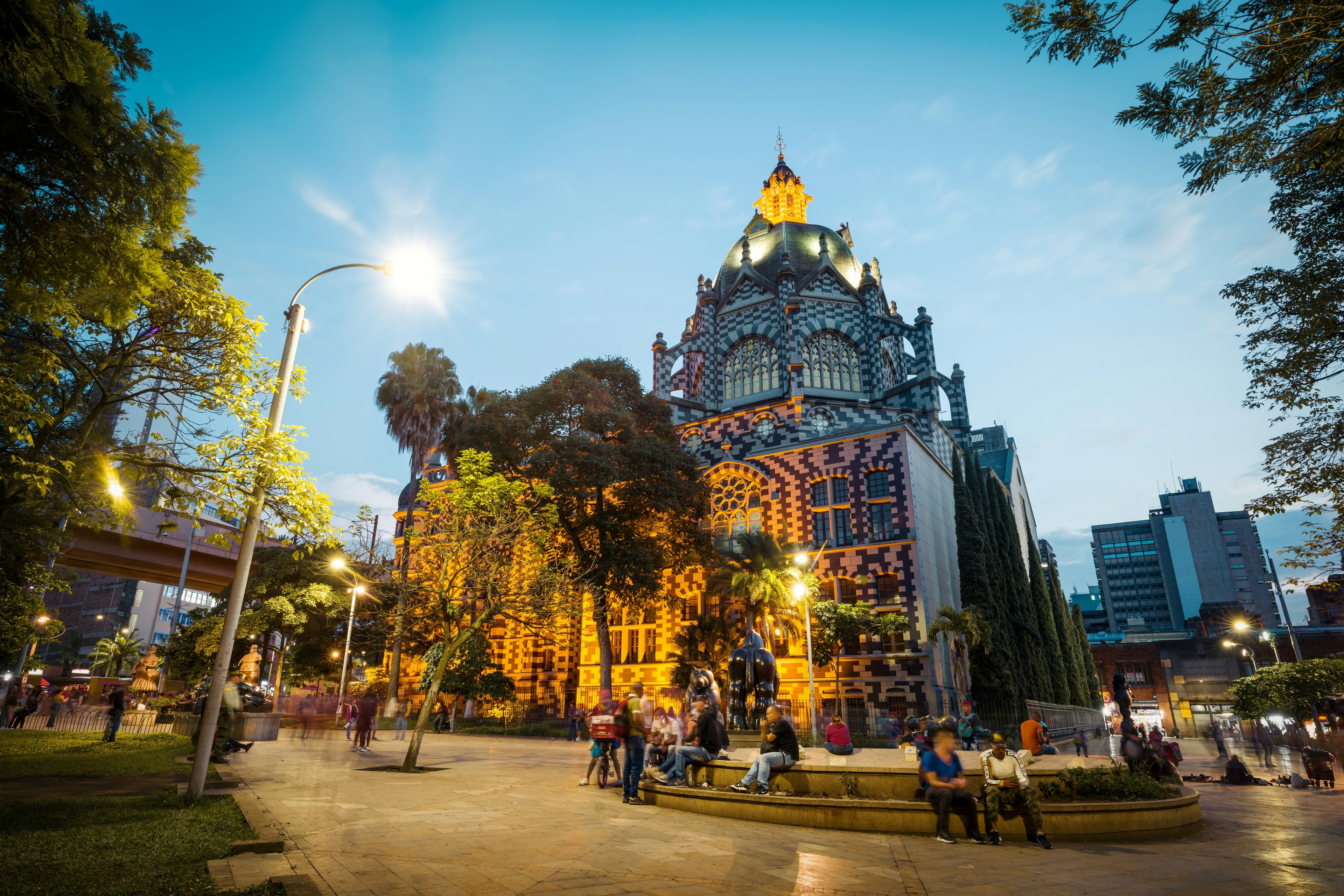 People gather in a plaza at dusk in front of an elaborately decorated church