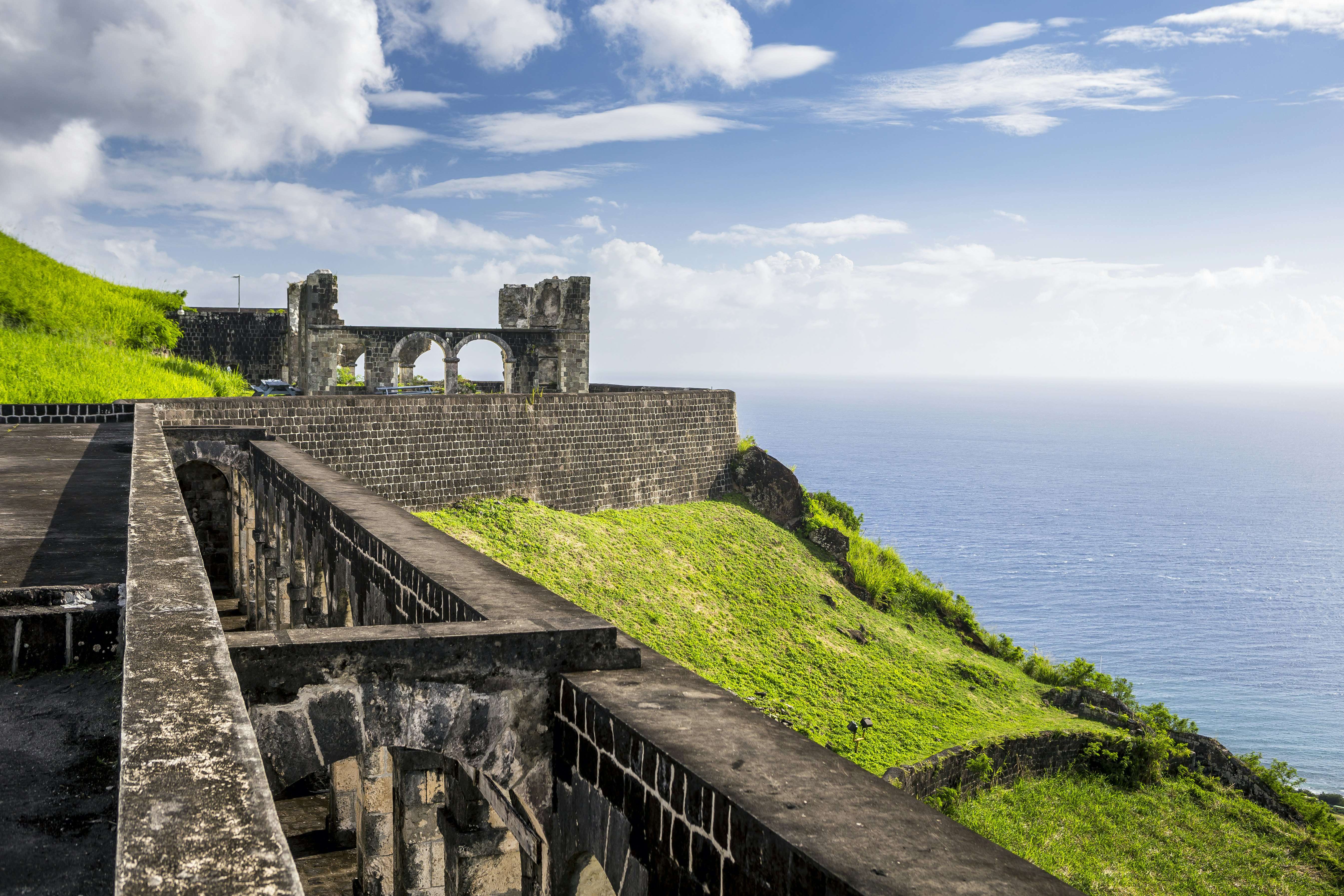 The dark gray stone of Brimstone Hill Fortress is starkly set off by green cliffs above a deep blue sea and a hazy horizon