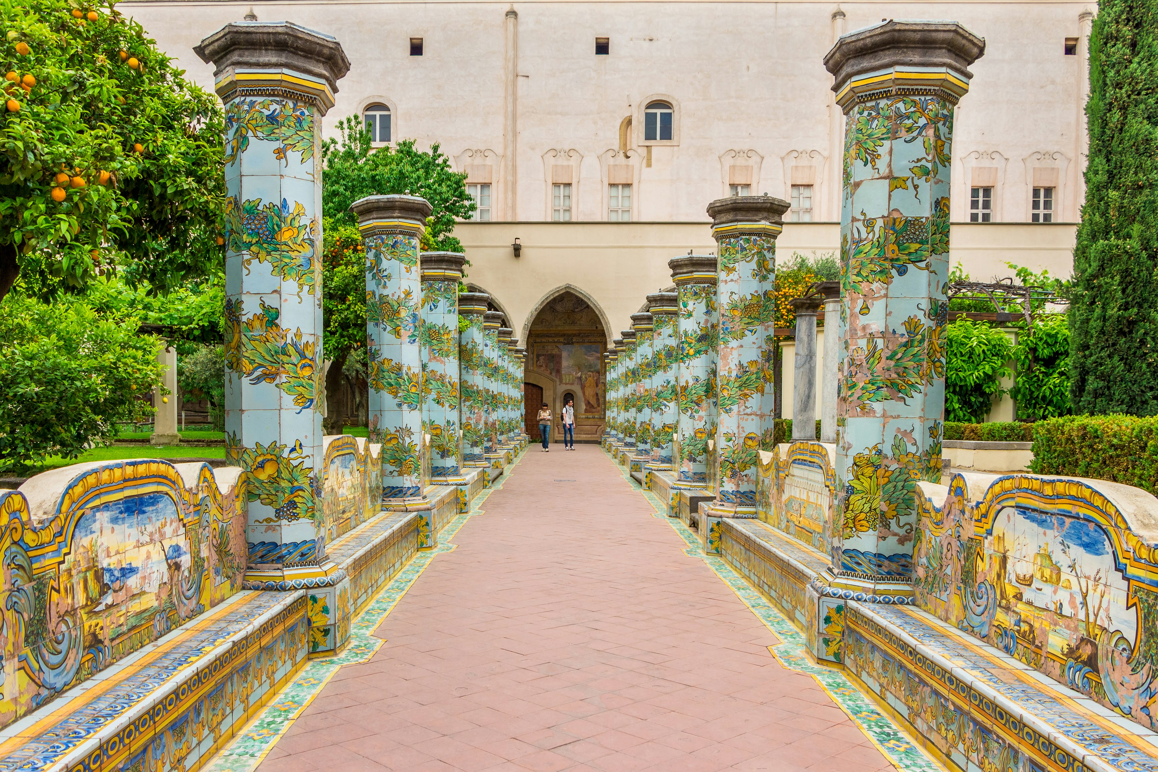 A row of columns plated with colorful majolica tiles leads to a Gothic archway at a monastery complex