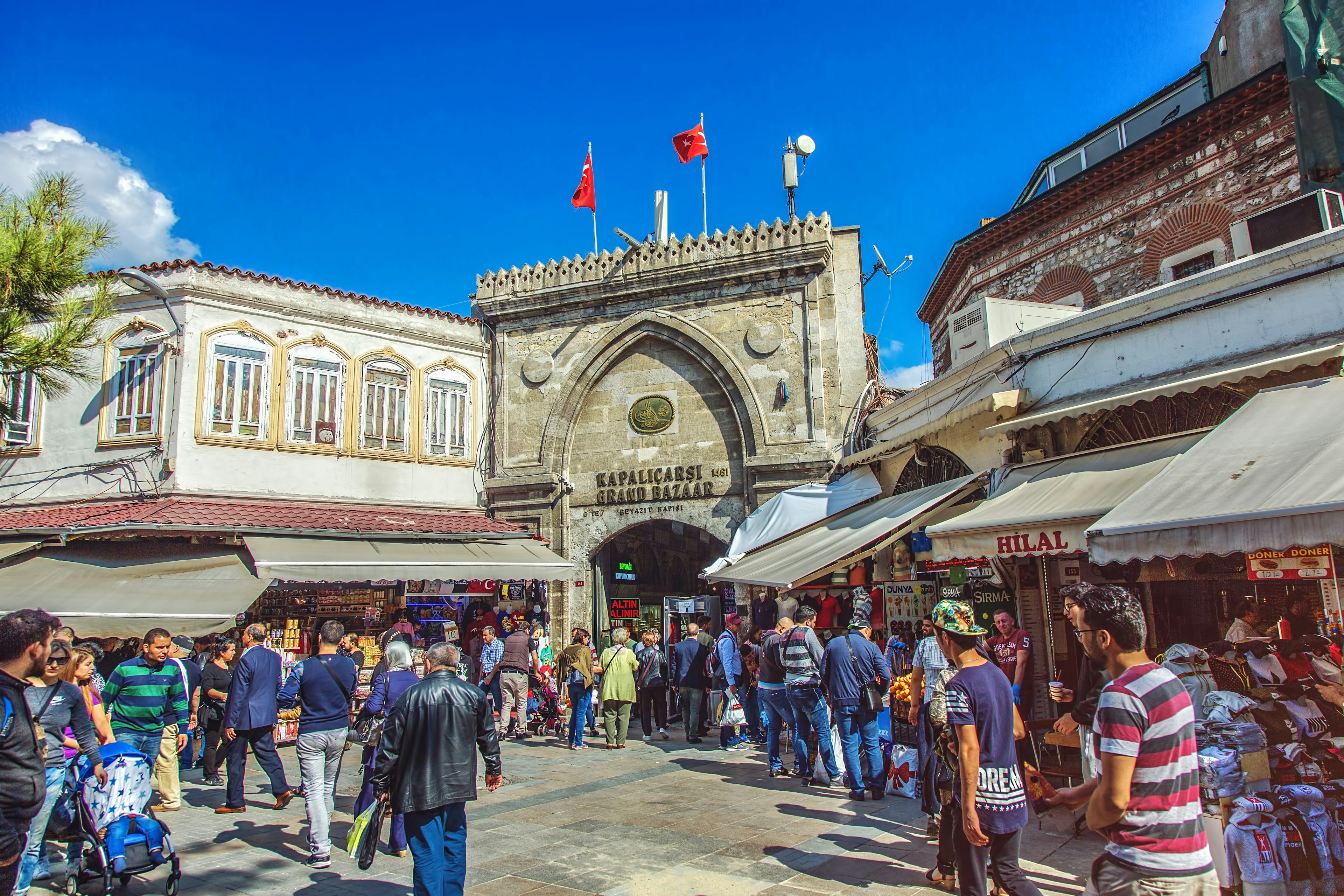 A series of market stalls near a busy gateway with a sign above it that says "Kapalcarsi Grand Bazaar"