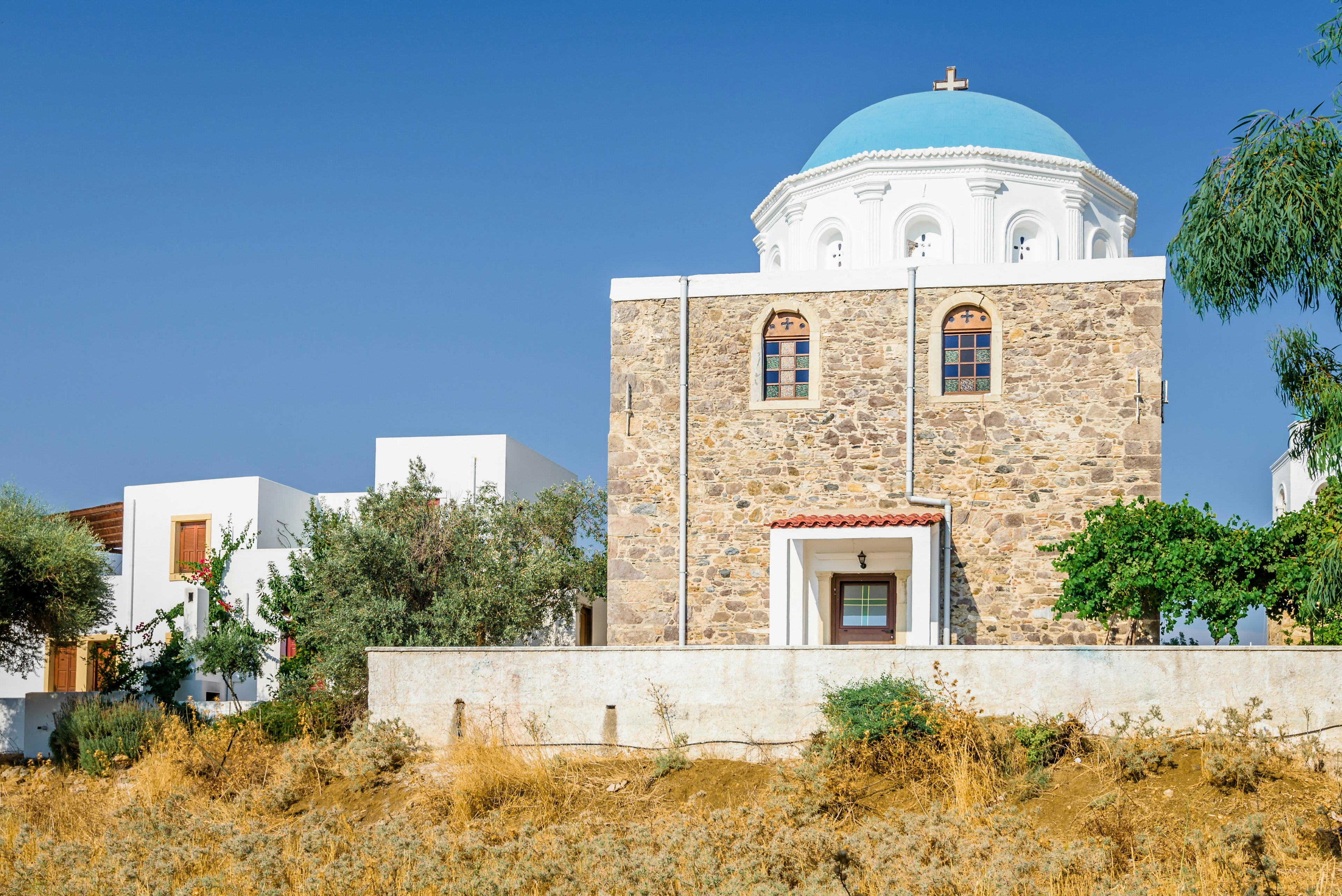 Holy greek stone church with white blue dome church in Evangelistra Asfendiou with cross over a blue sky.