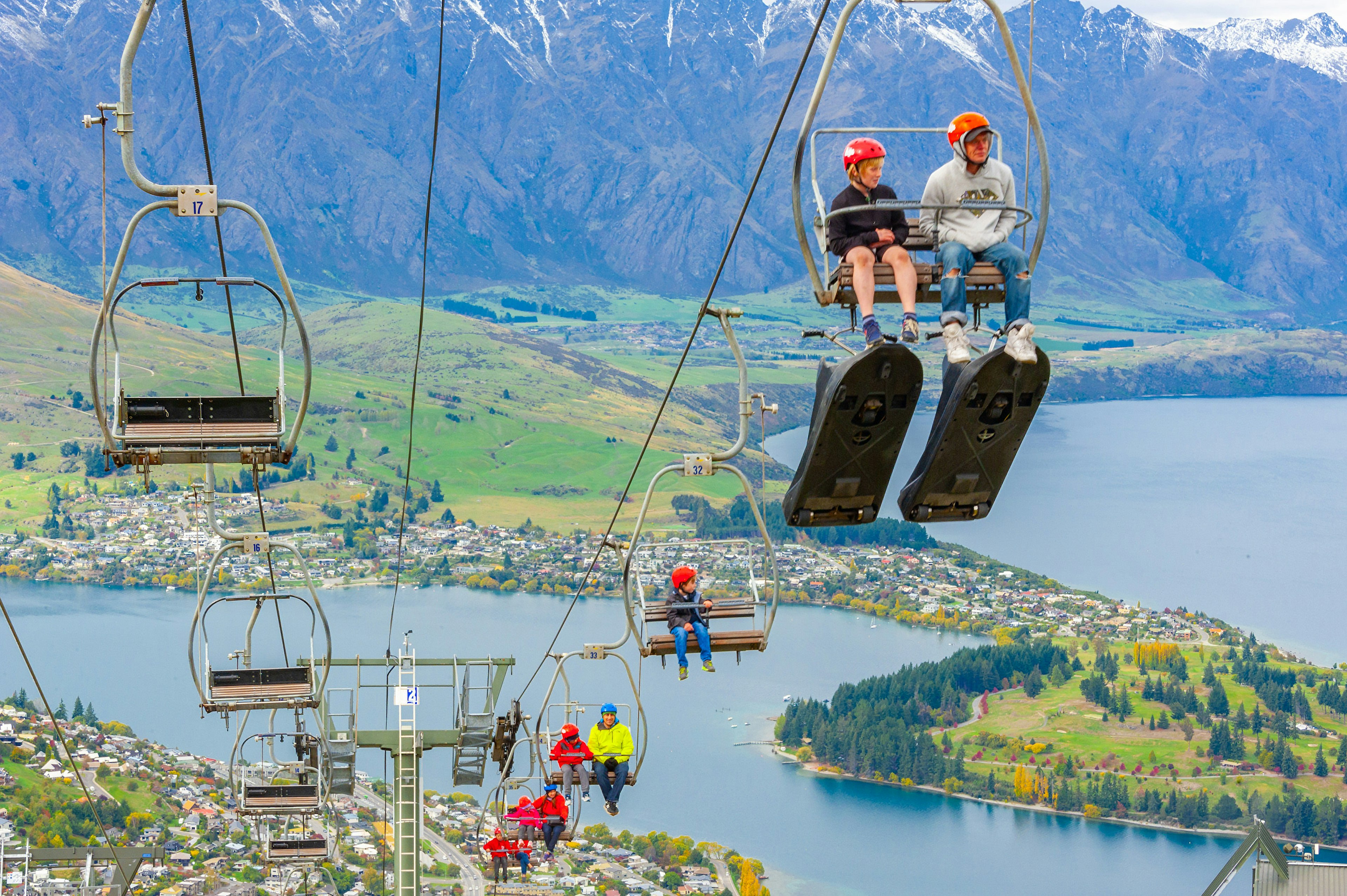 People seated on a cable chair lift, heading to the top of the hill for luge rides in Queenstown.