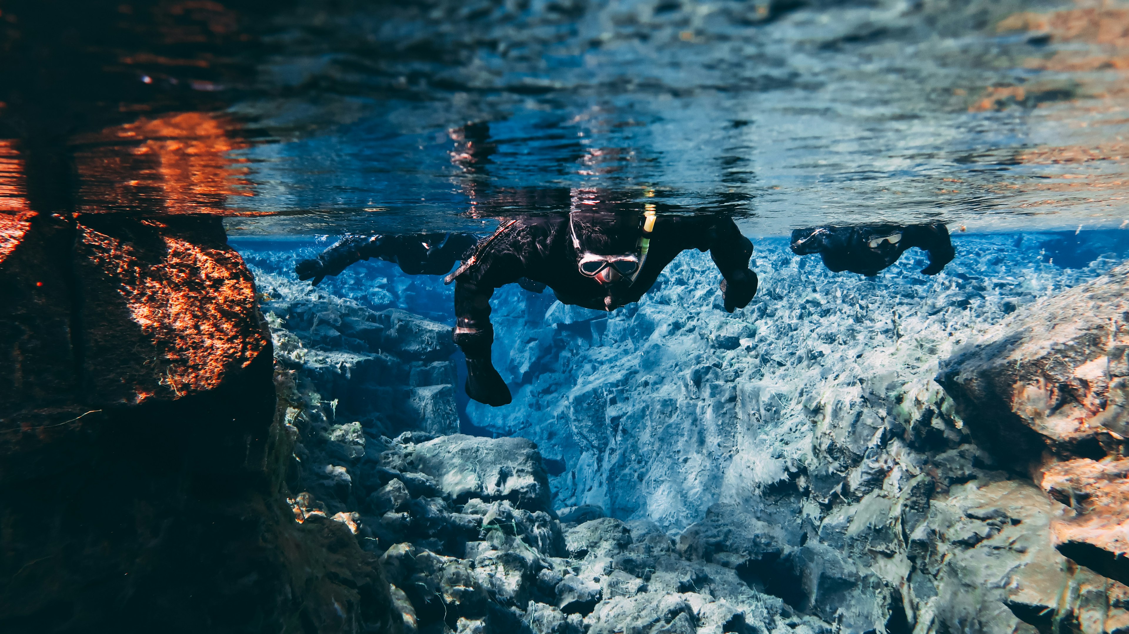 Two snorklers in clear water gazing down on rock formations