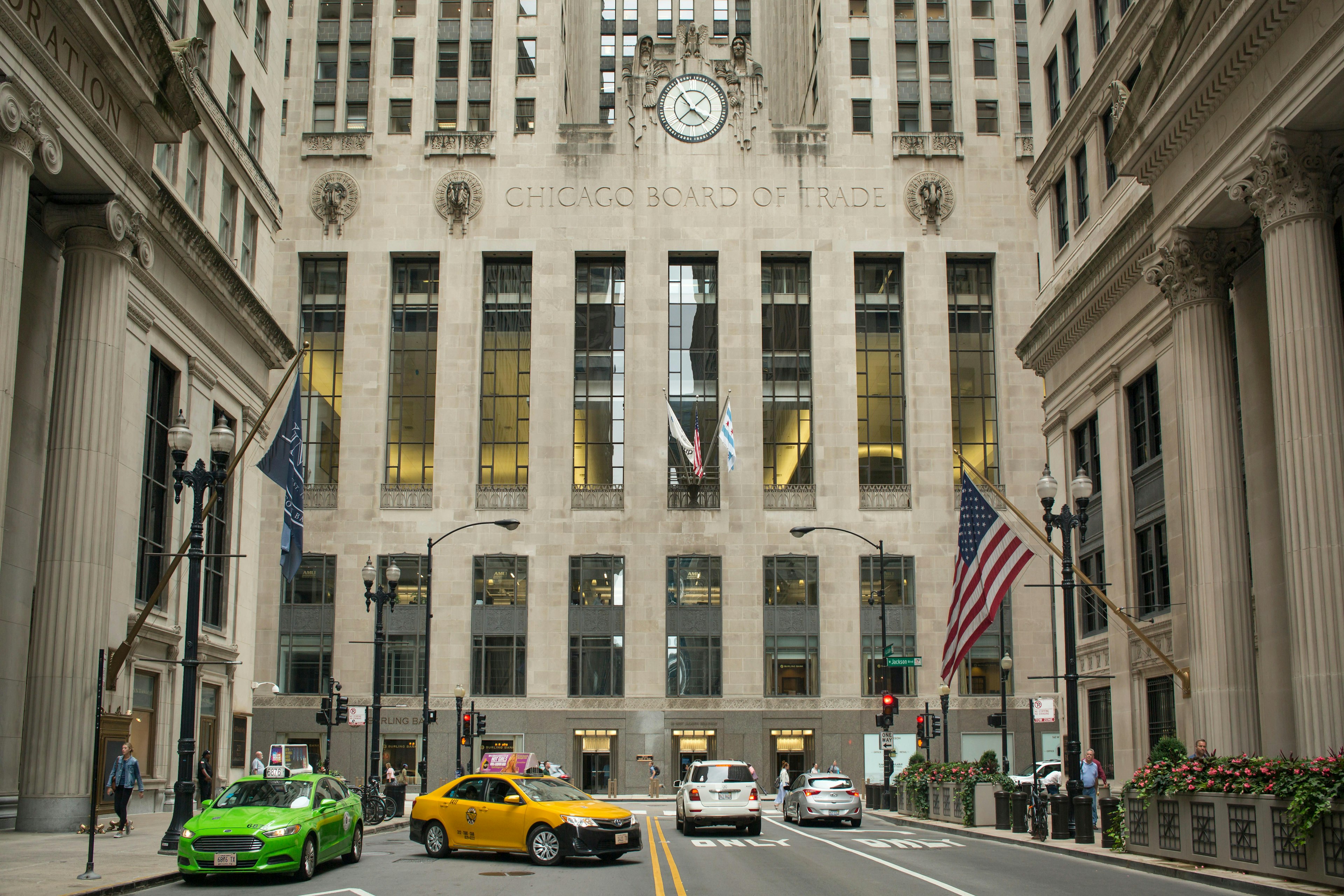 Facade of the Chicago Board of Trade with two colourful taxis and the American flag.