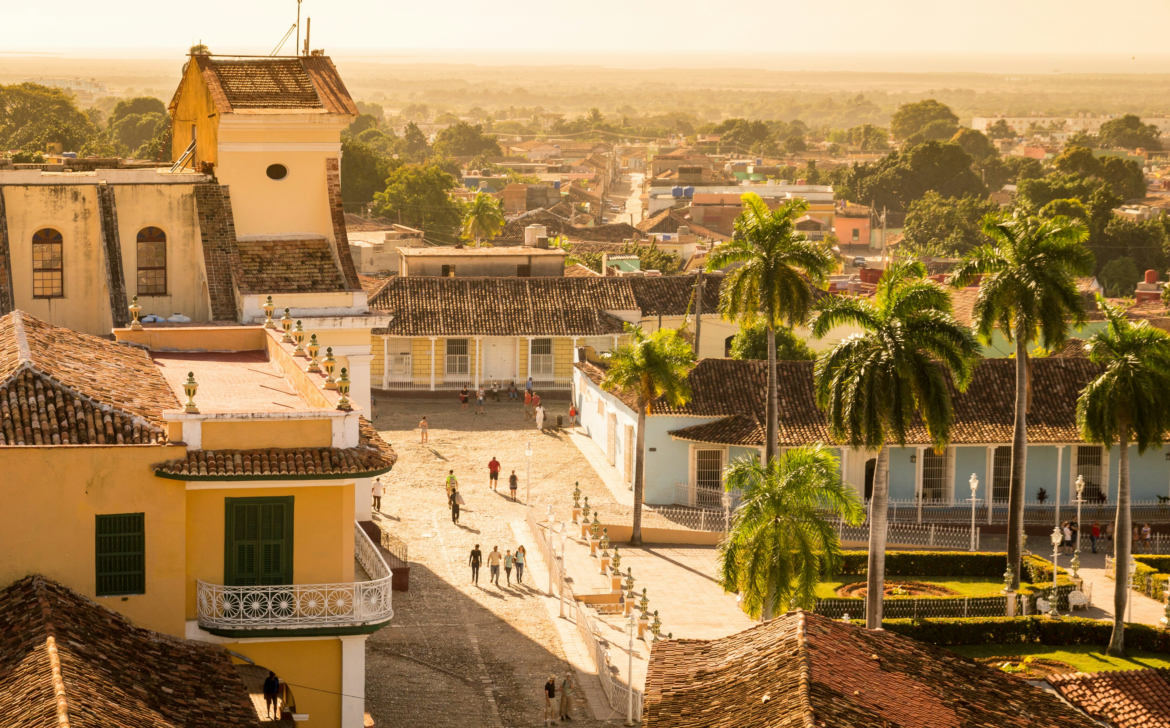 People wander on cobbled streets among colonial buildings in a town center