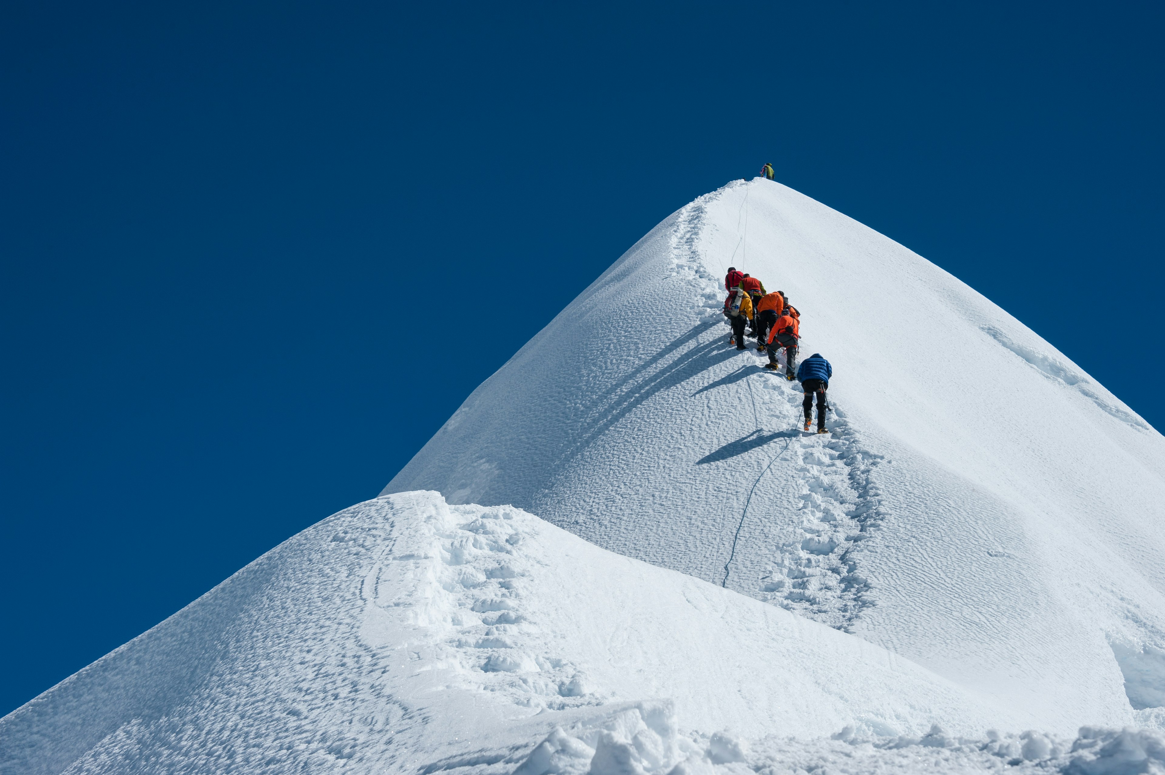 A group of hikers climb up in a line along a snow-covered peak in Nepal.