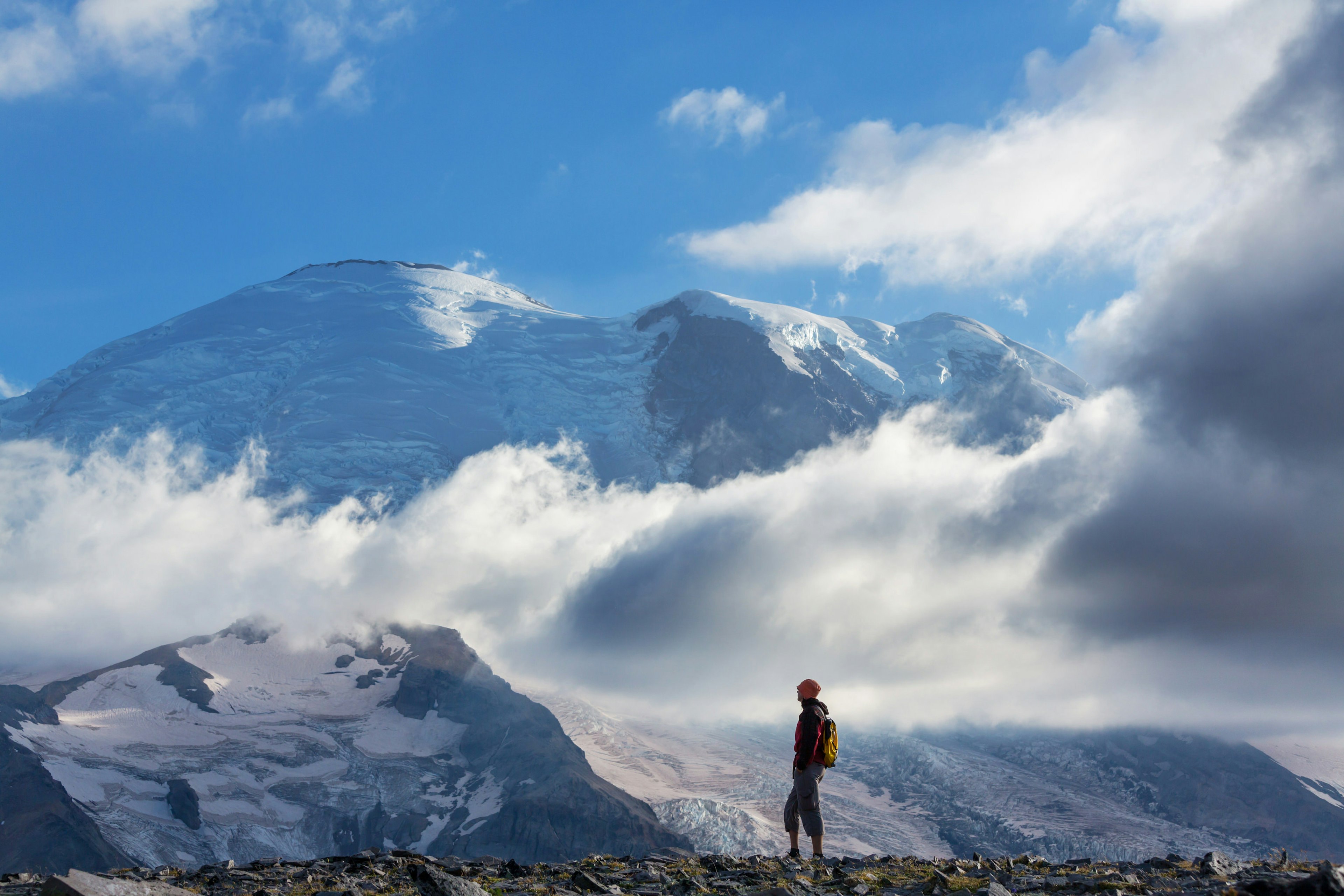 Hiker pauses on a trail to look at the snow-capped peak of Mt Rainier.