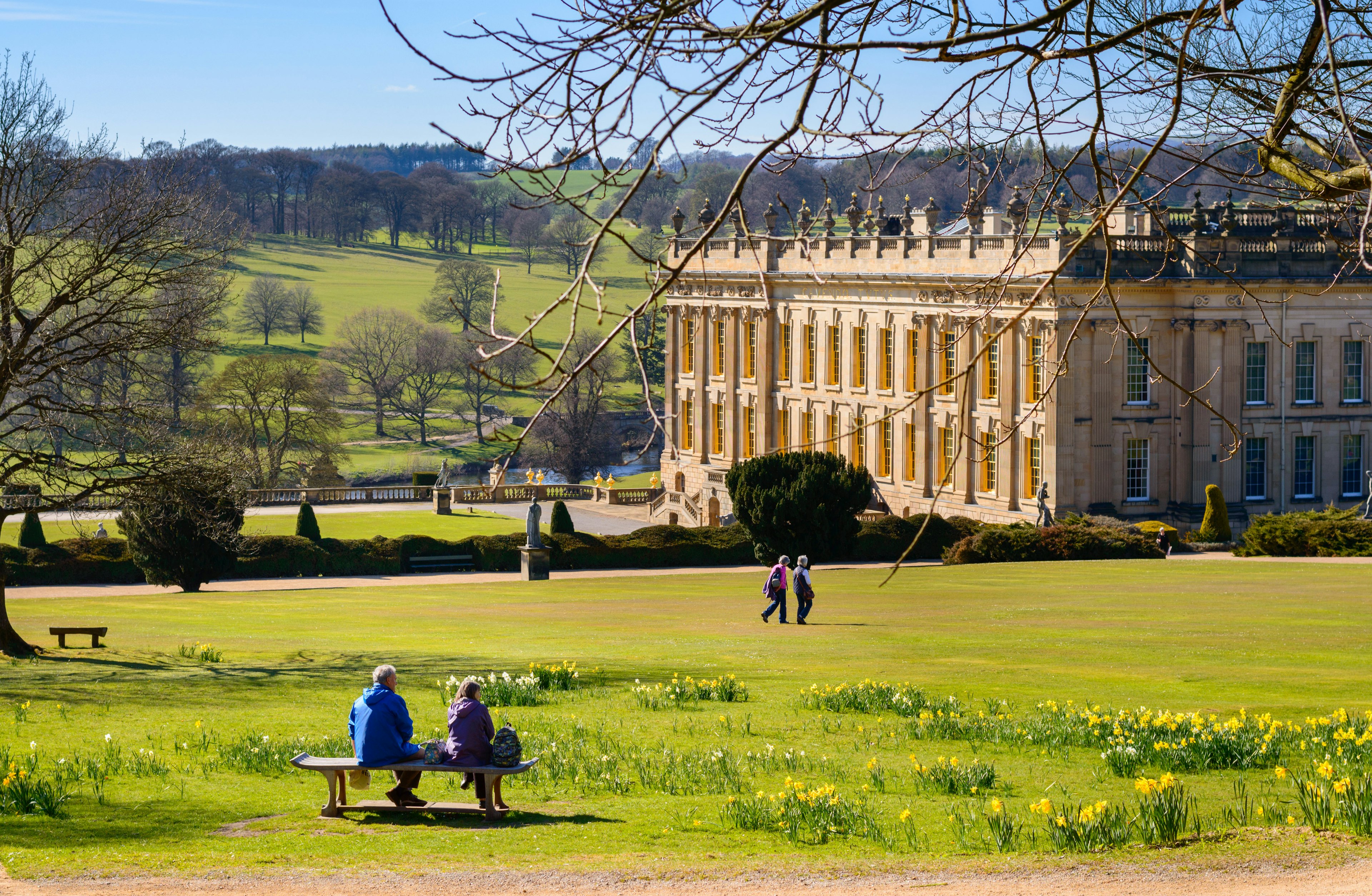 A middle aged couple sit on bench in gardens of Chatsworth House.