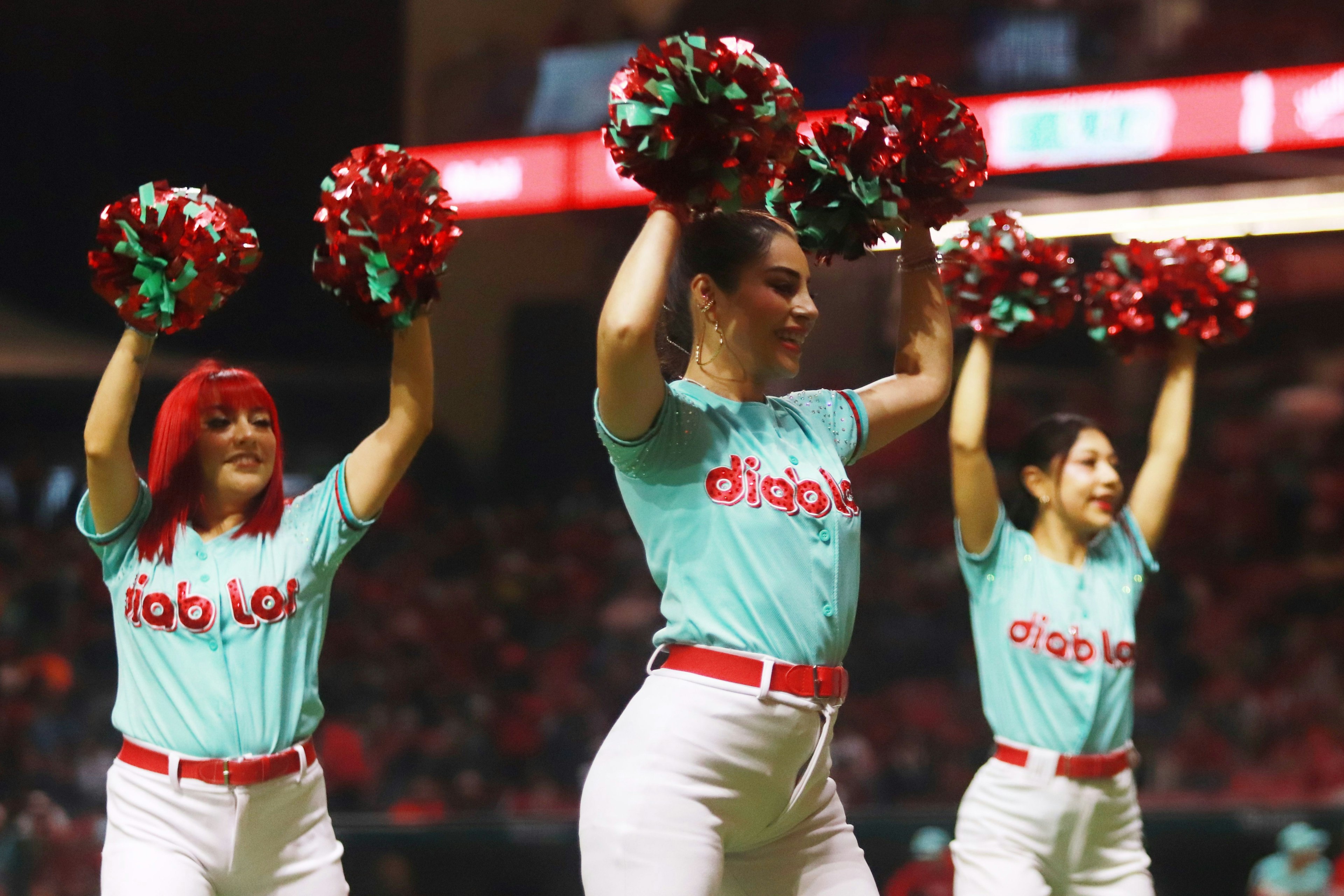 Cheerleaders in turquoise t-shirts and white trousers wave pom-poms in the air during a stadium performance