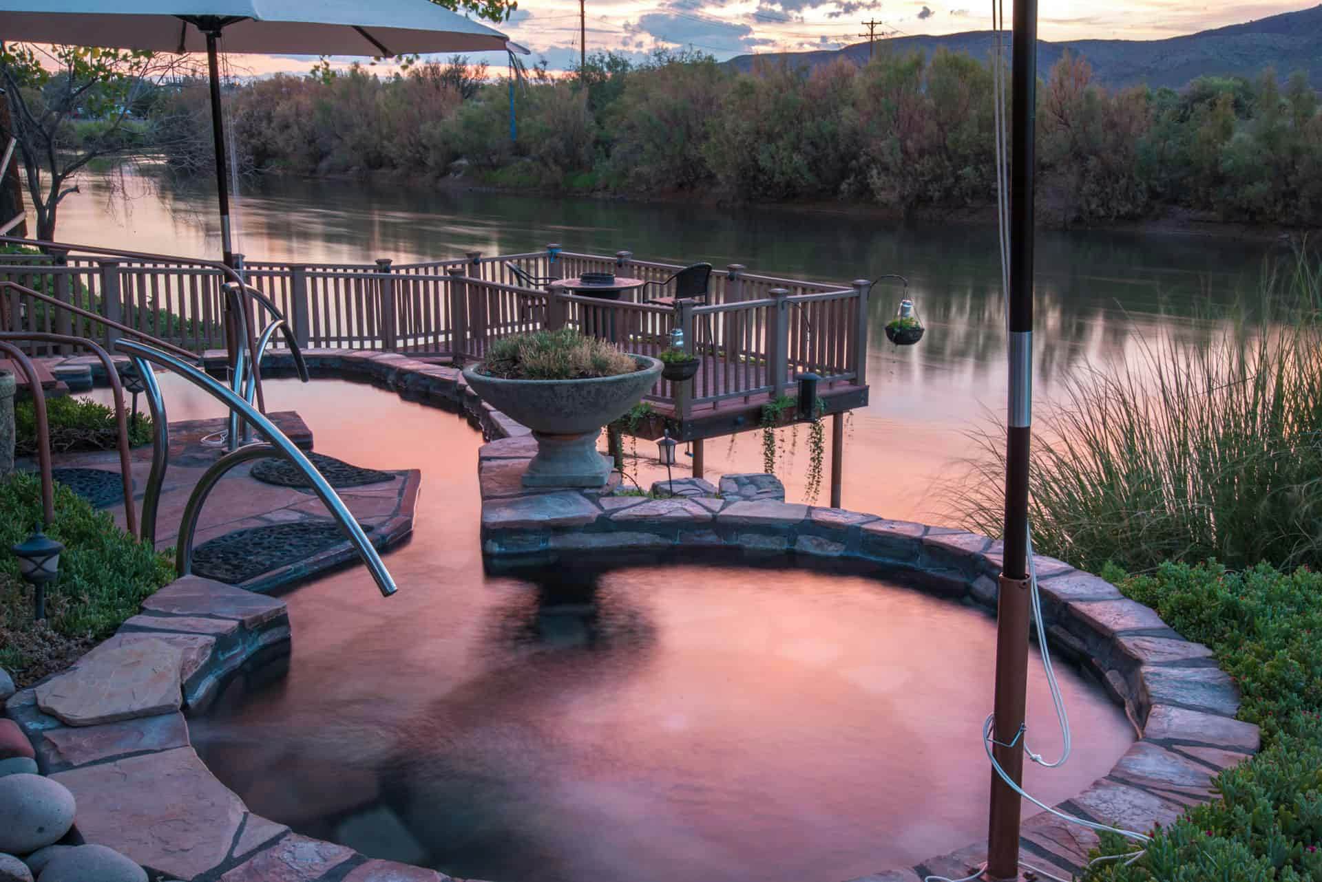 A small round pool right beside a river glowing pink in the twilight