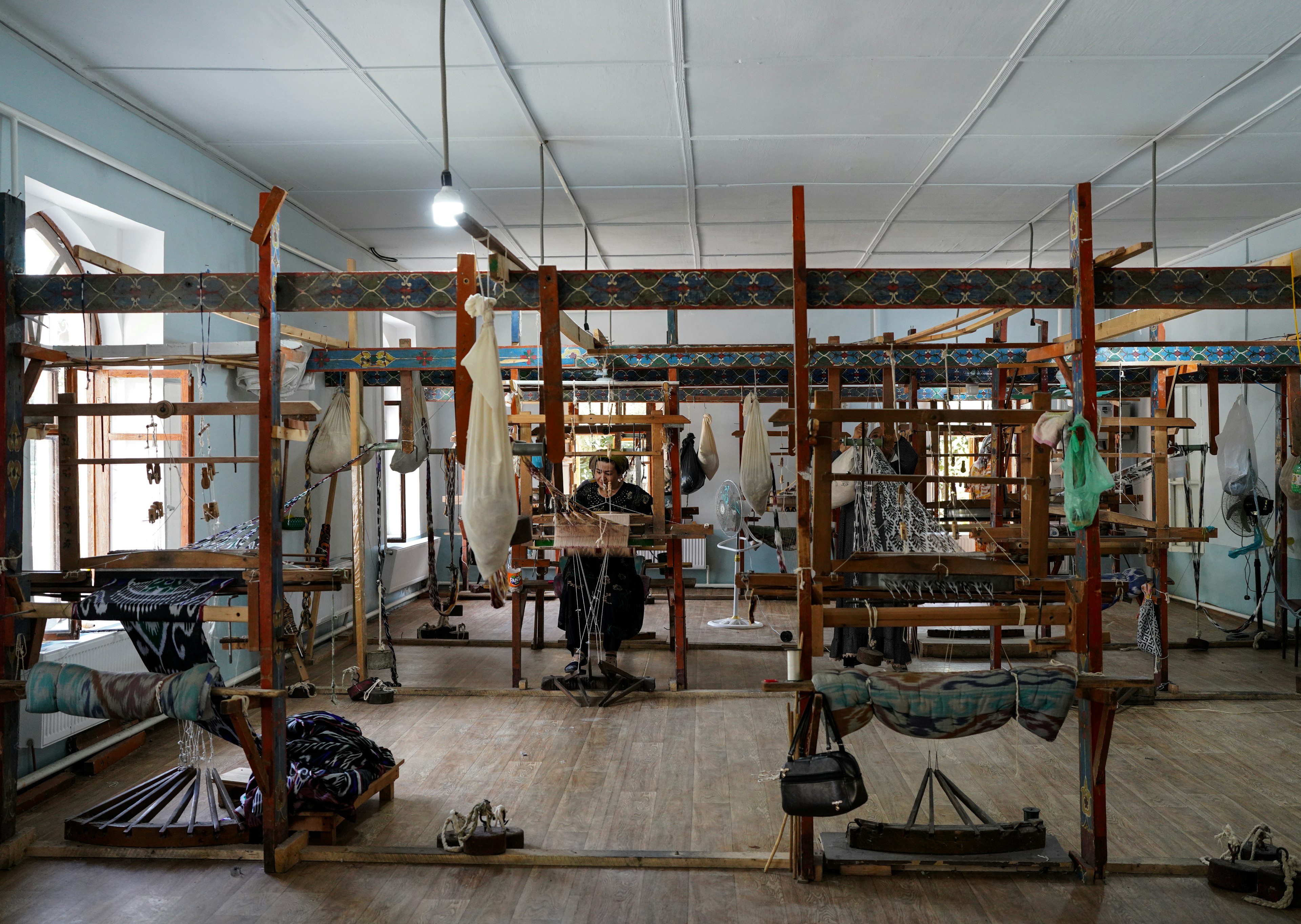 Silk looms on a factory floor. A woman sits at one working away with silk