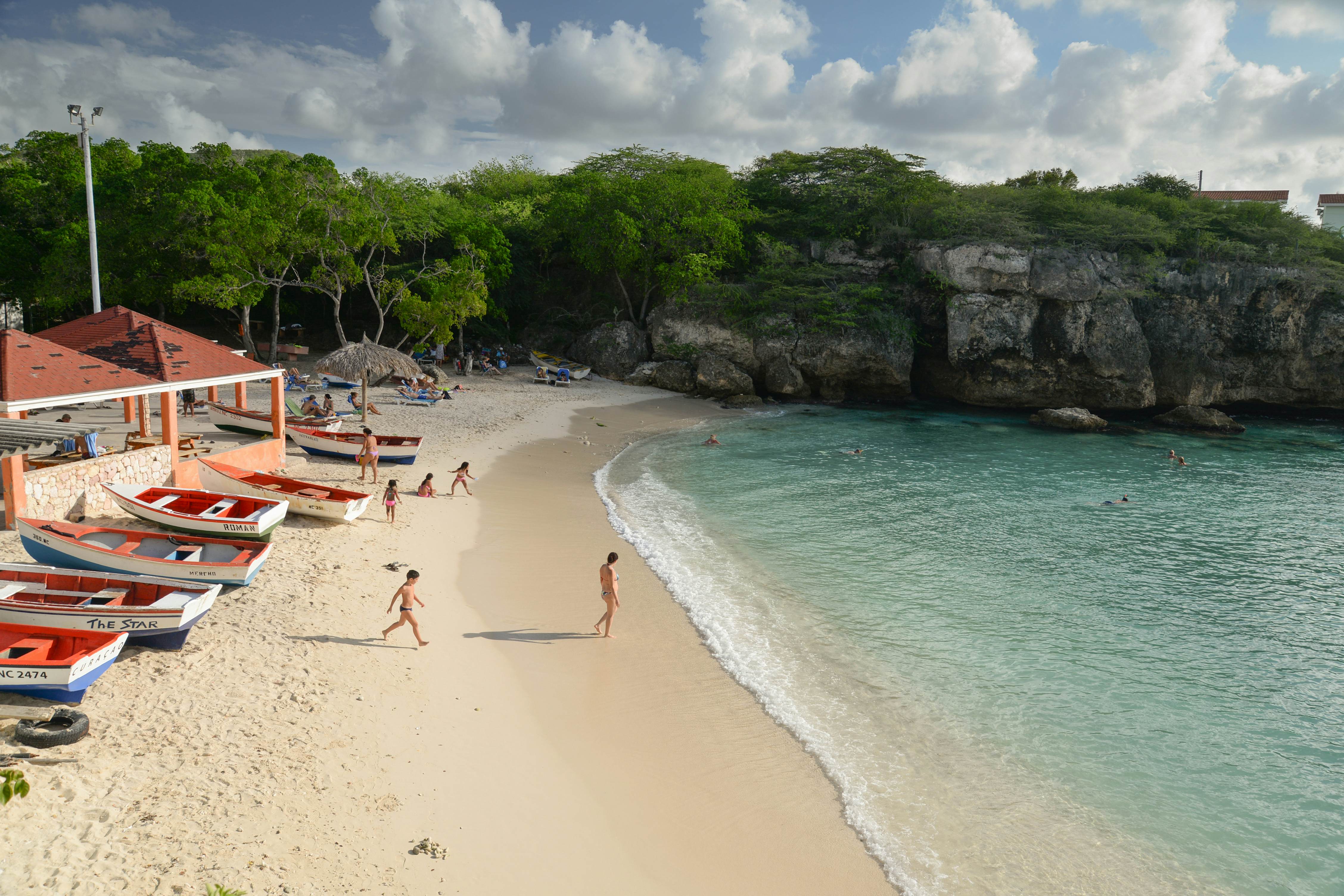 Kids play on a sandy beach backed by a row of small wooden boats