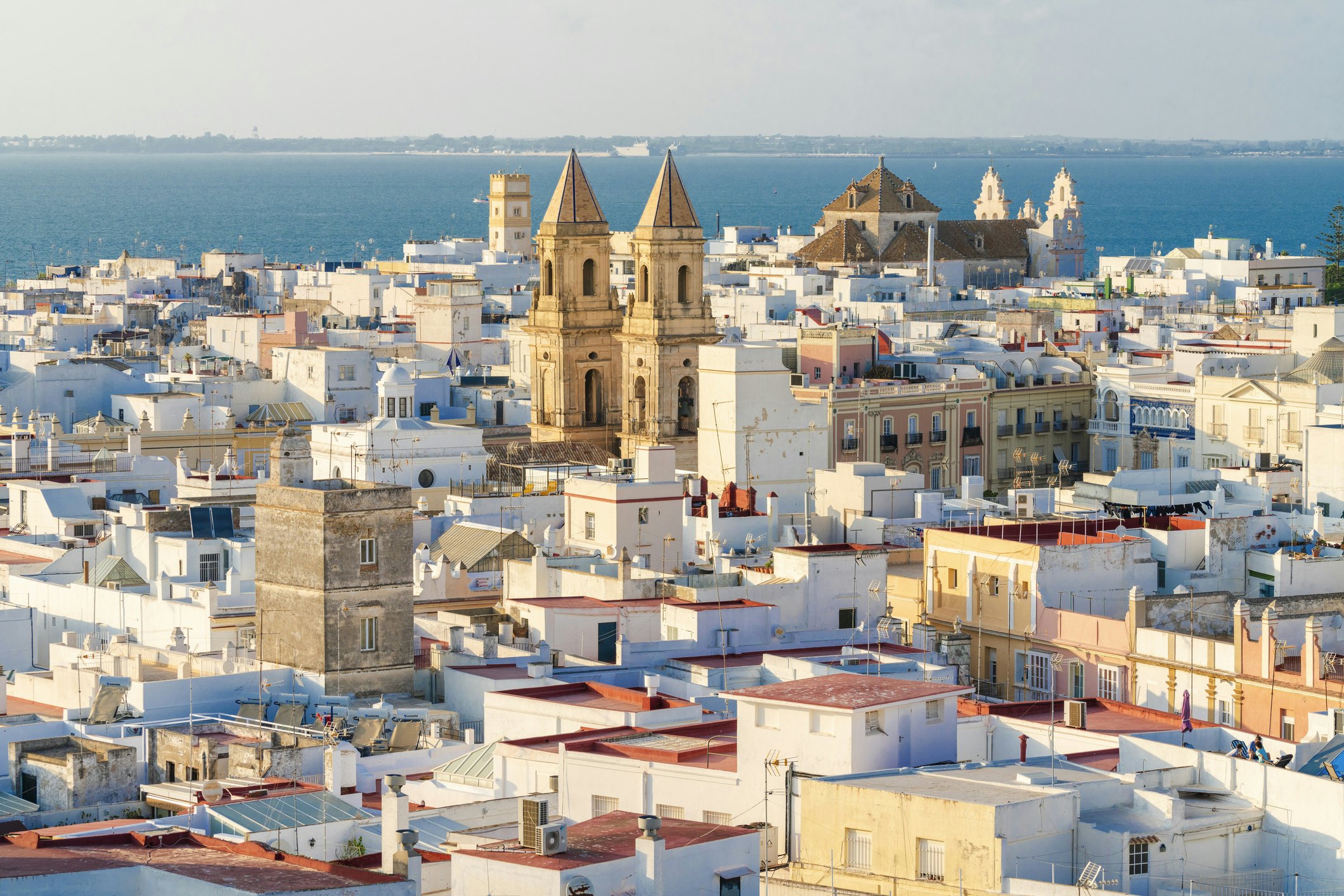 View over the rooftops of a low-rise ocean-side city with several tall church towers.