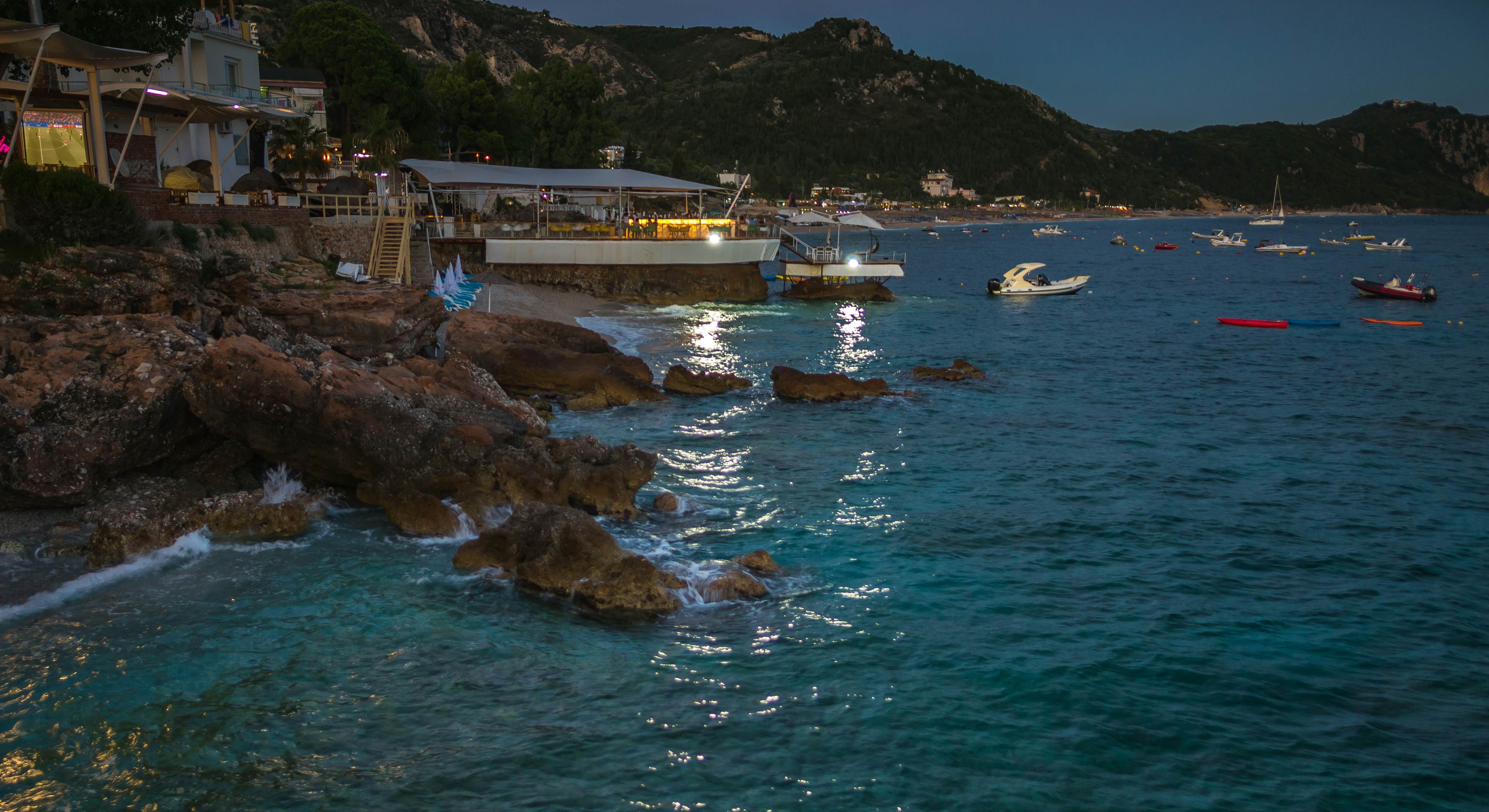 A rocky cove is pictured at night, with lights from a restaurant illuminating boats moored in the water.