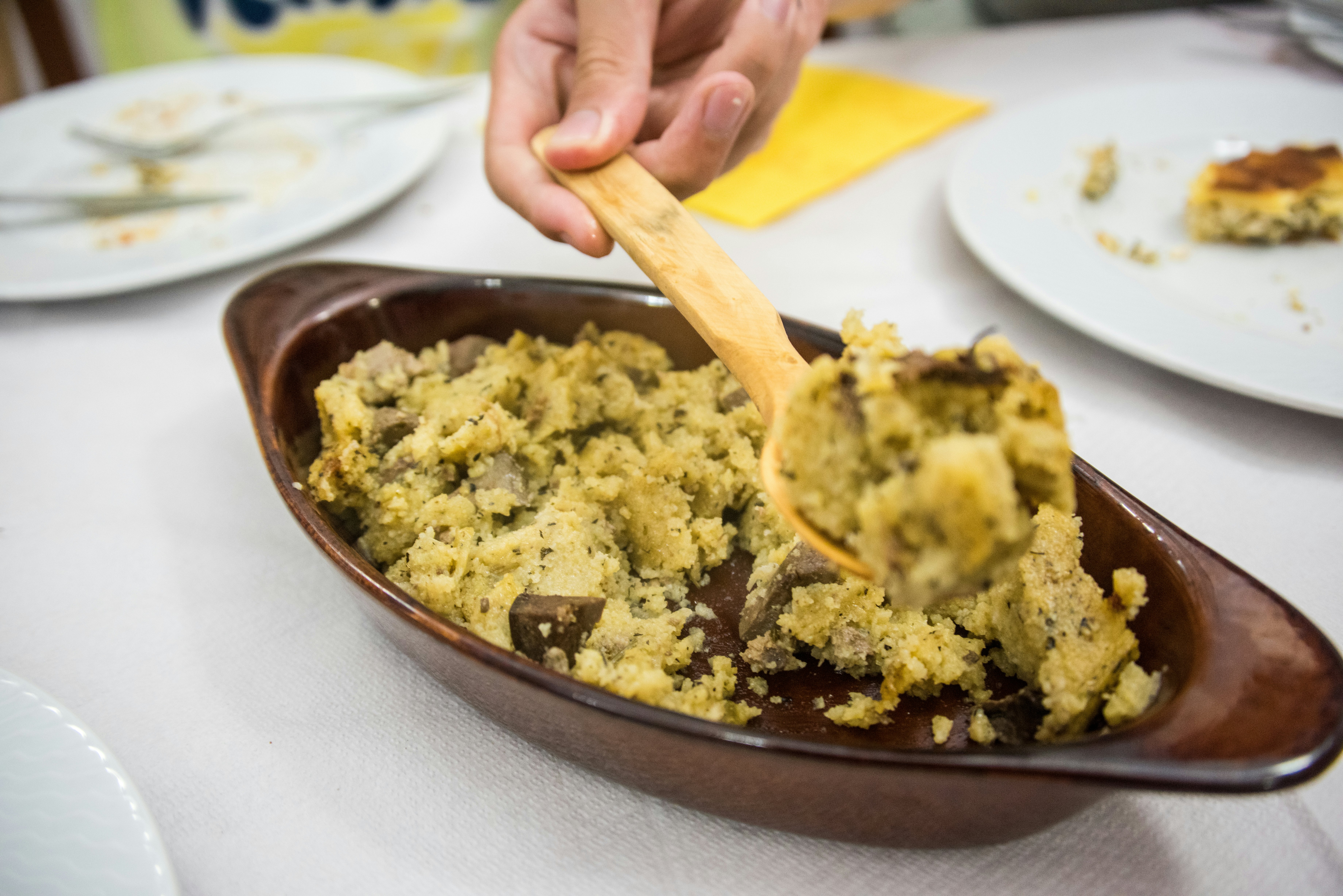 A person spoons from a dish a serving of Albanian harapash, made with cornflour, goat butter, olive oil, milk, and cottage cheese, mixed with lamb offal.