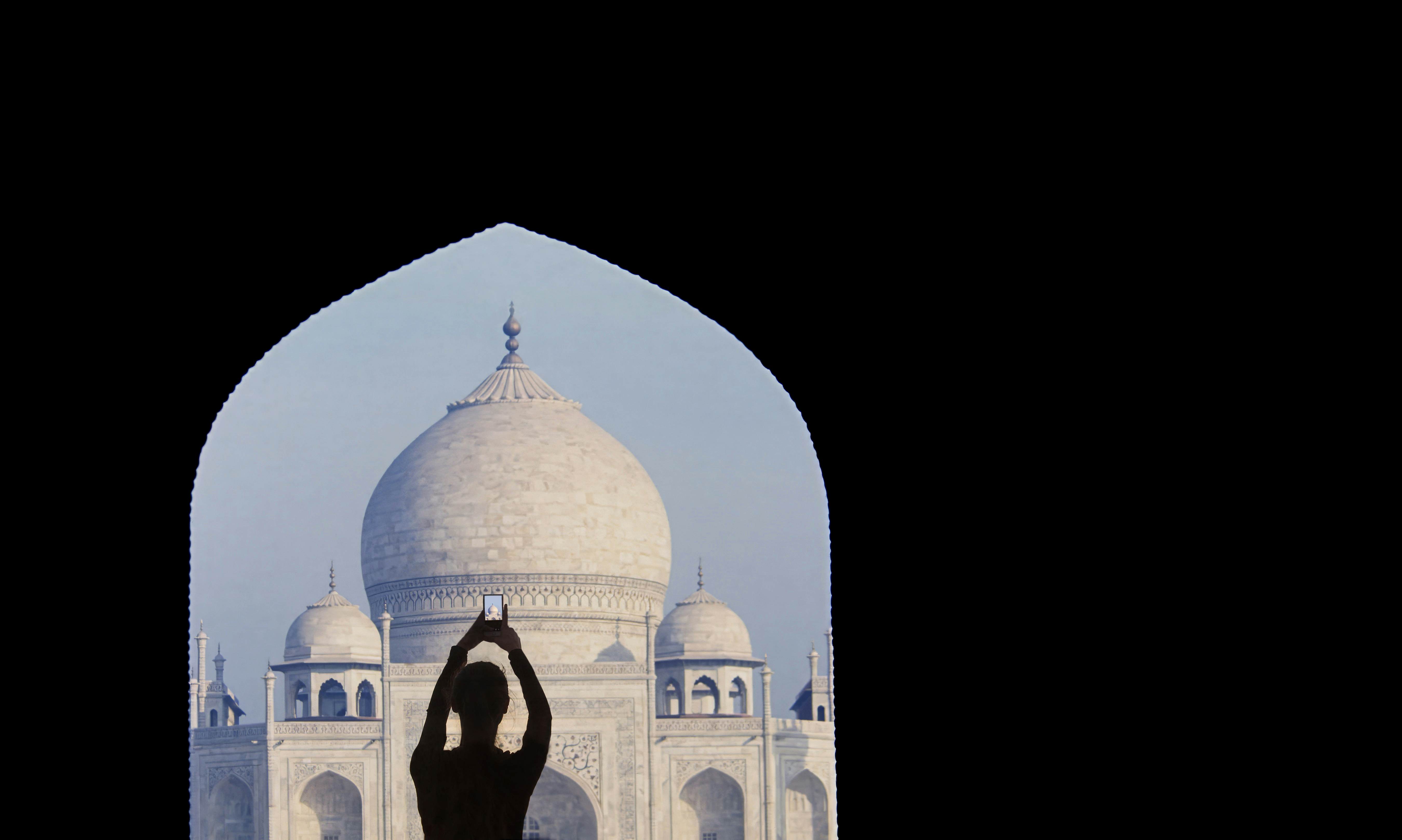 A person seen in silhouette raises their phone to photograph the domes of the Taj Mahal in the morning light, Agra, Uttar Pradesh, India