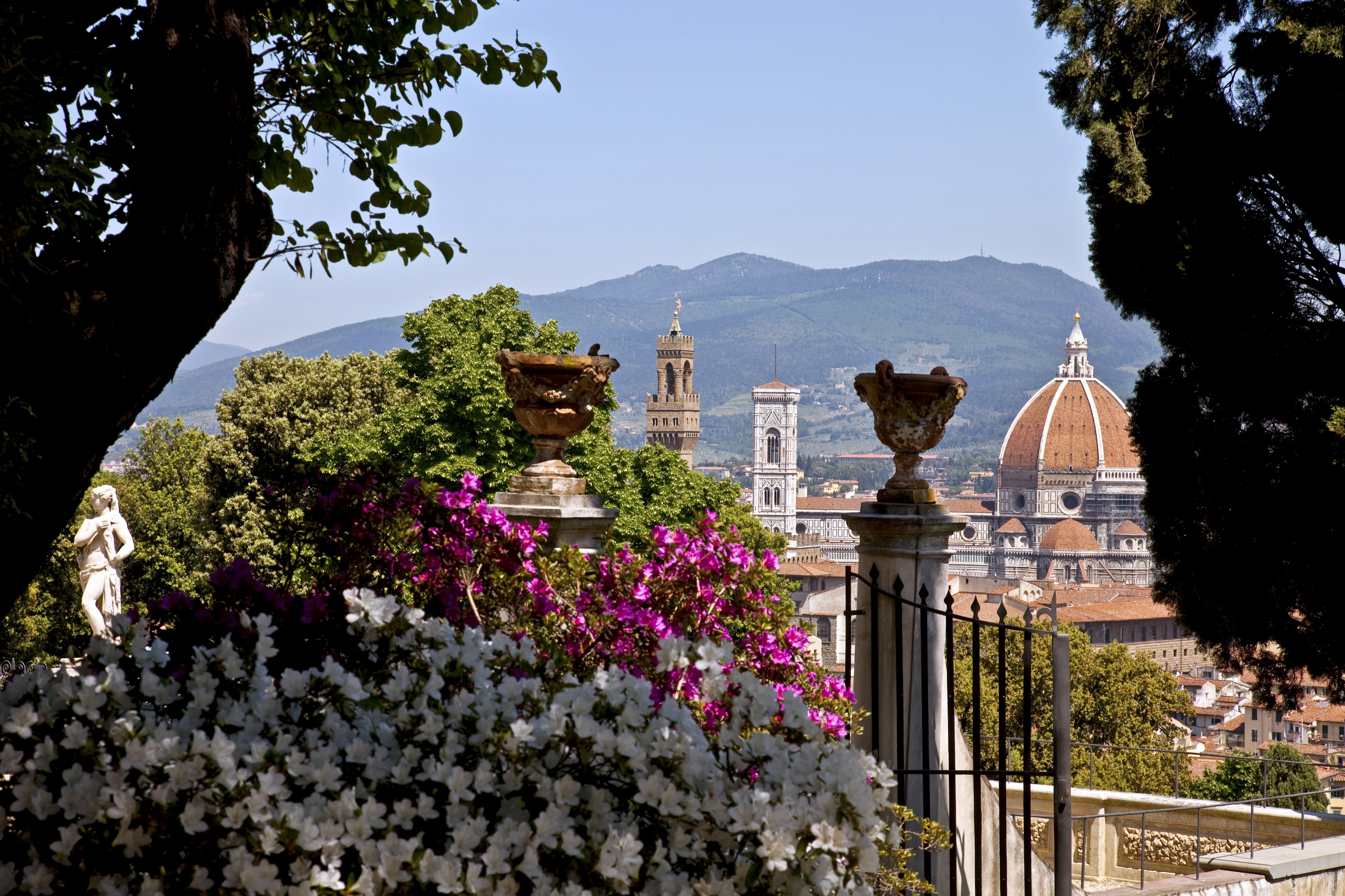 Trees bloom with springtime flowers in front of a red-brick cathedral dome with a square church tower