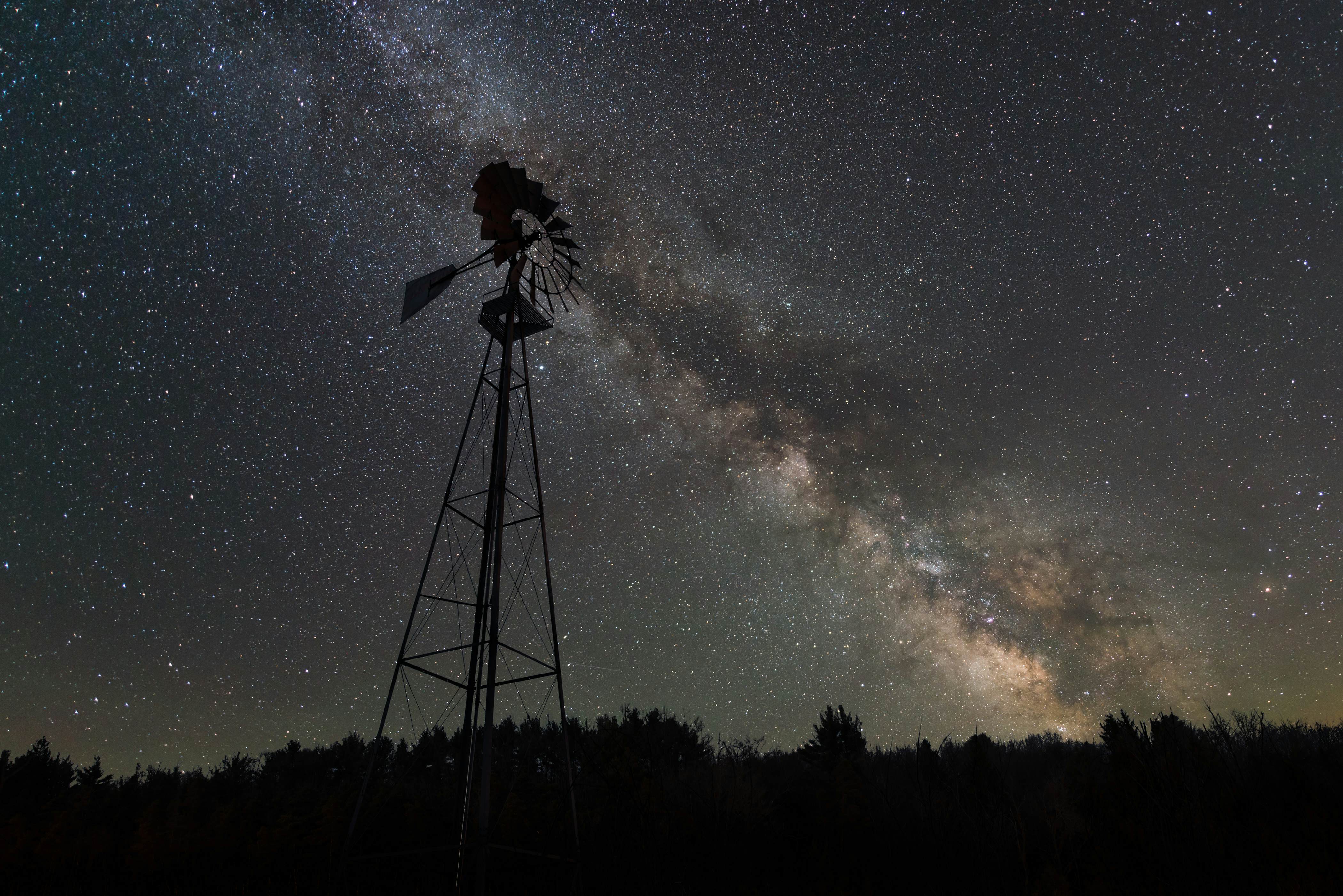 Silhouette of a windmill against a night sky with a blanket of stars