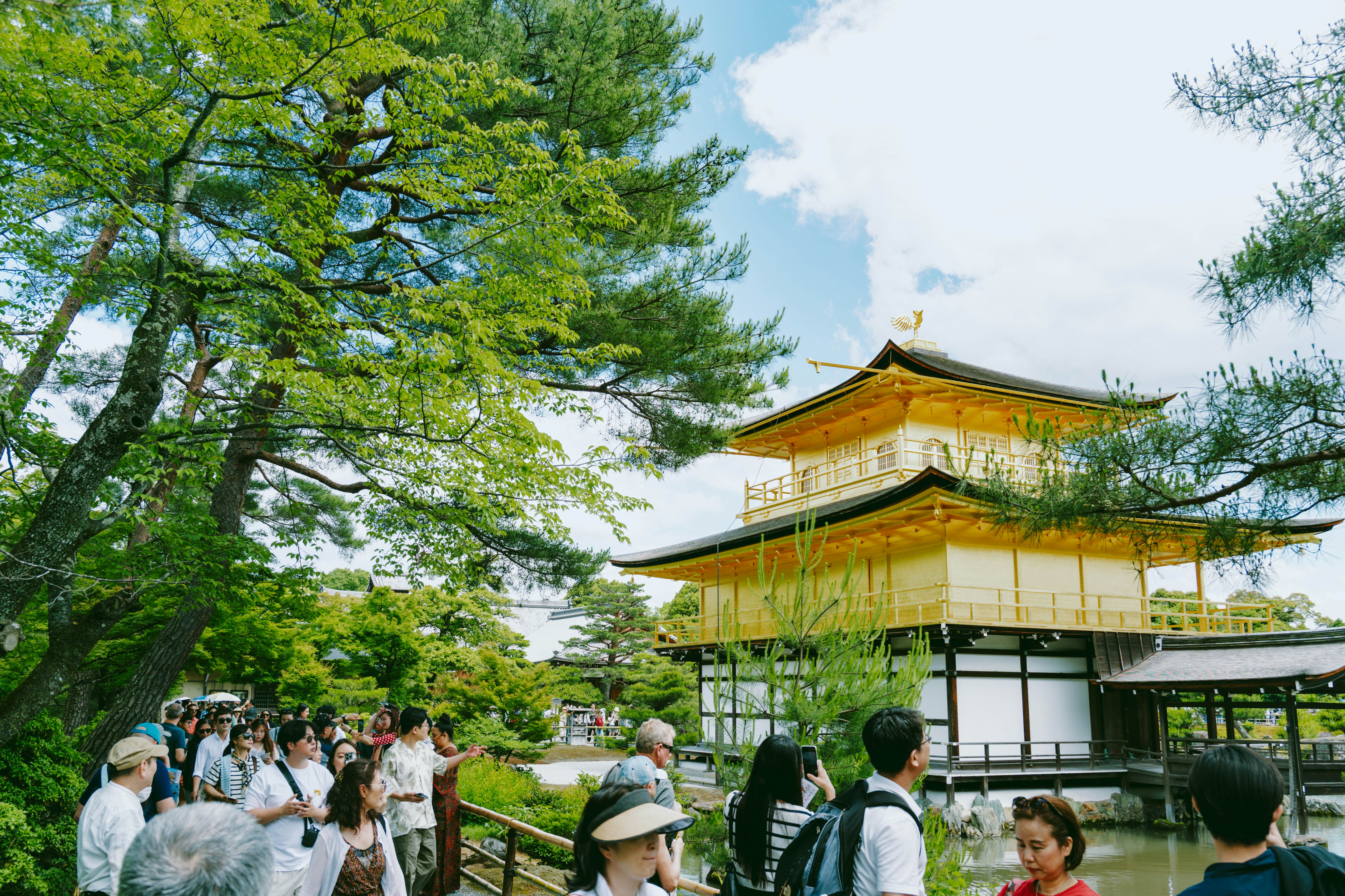 People walk past a lakeside temple with gold-leaf tiers