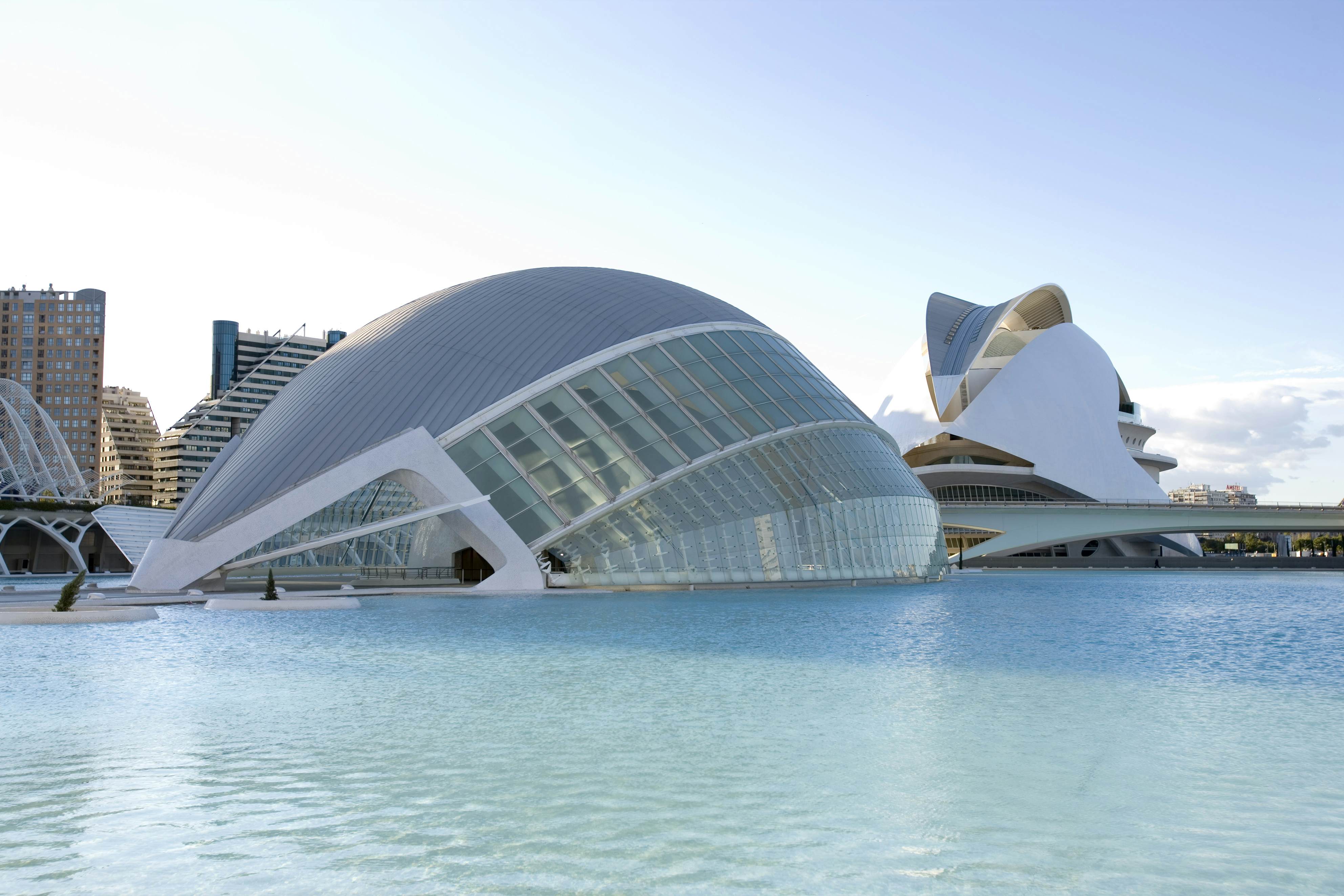 A strange hemispheric building appears to rise out of blue water, with buildings in the background.