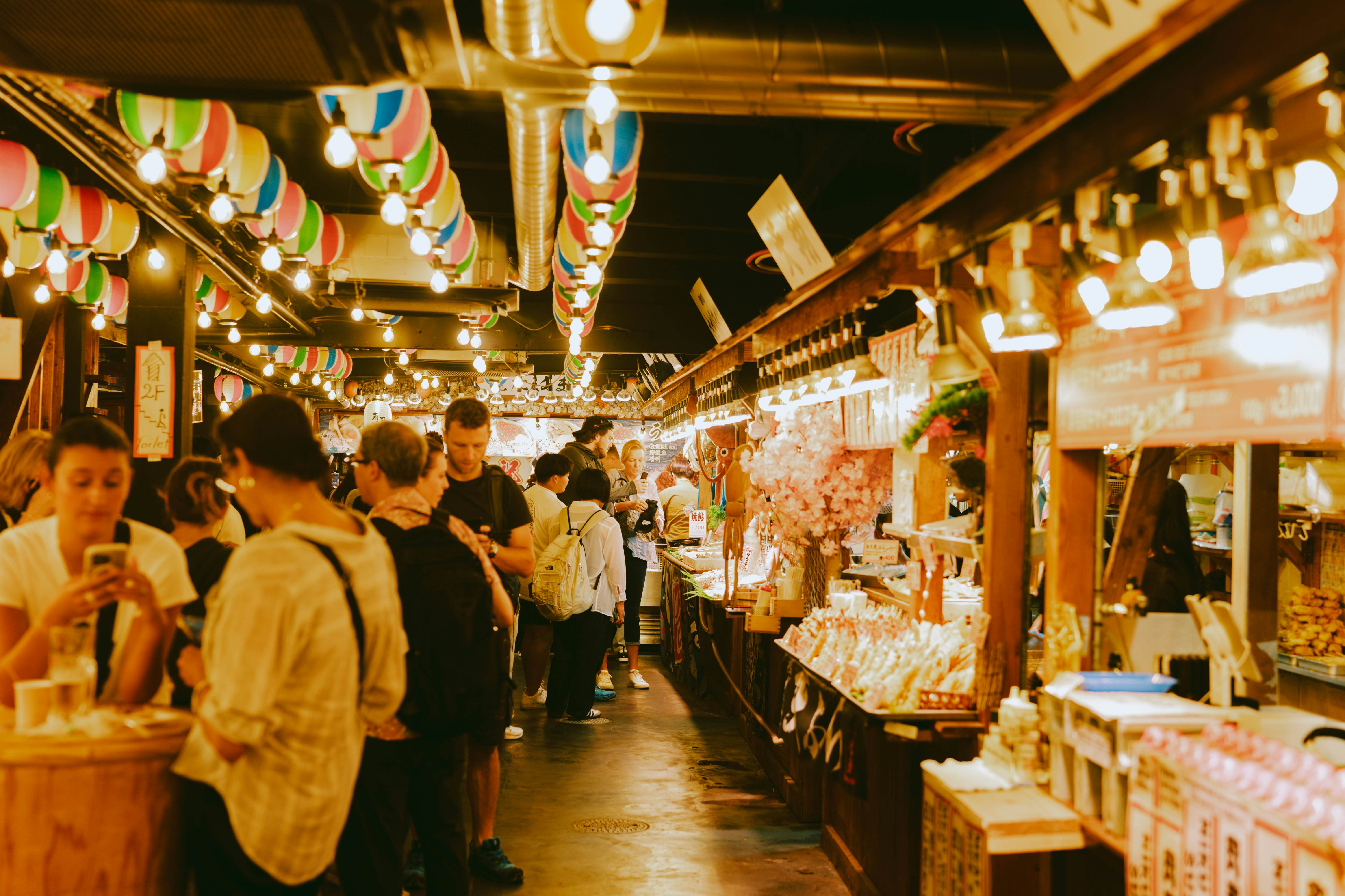 People at a market at night with strings of lights hanging above food stalls