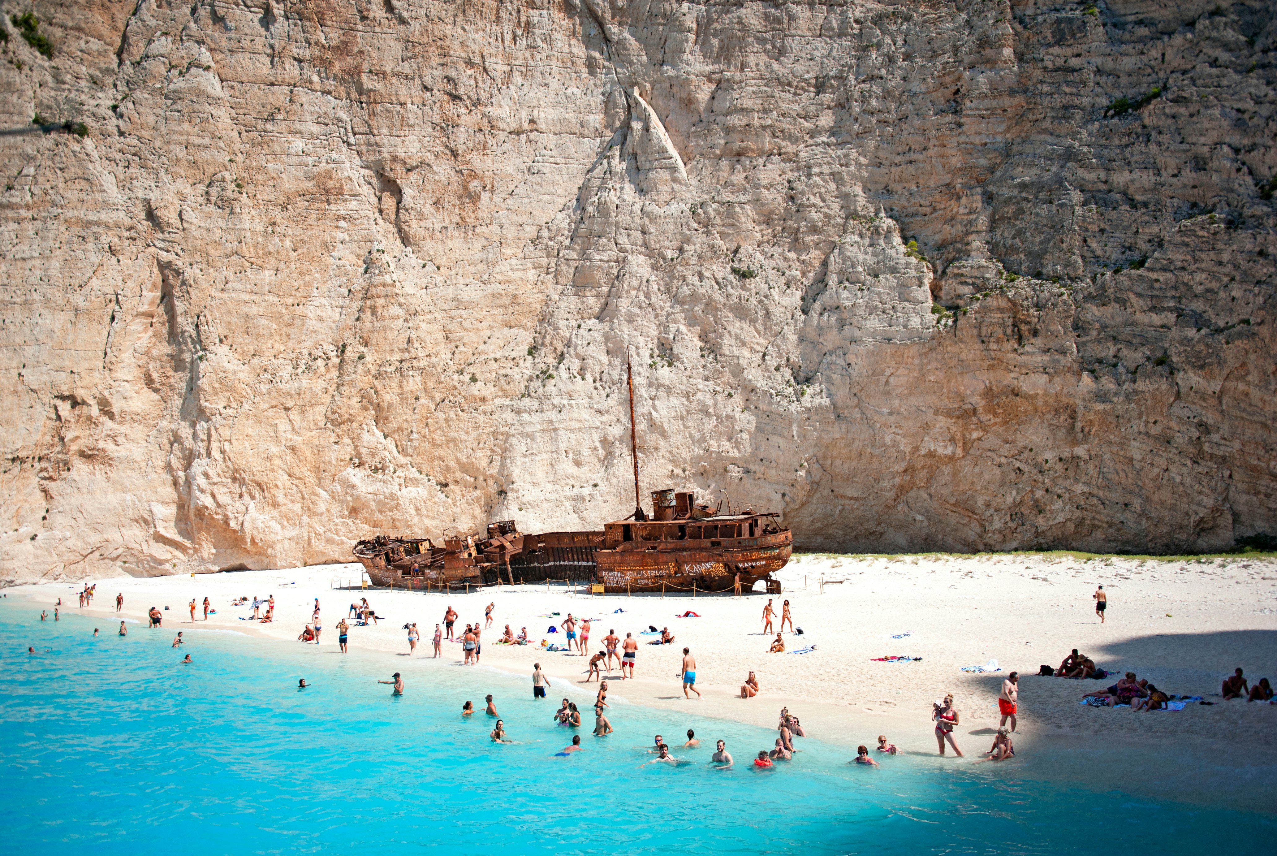 People swimming and taking photos on Navagio Shipwreck Beach, Zakynthos, Greece.