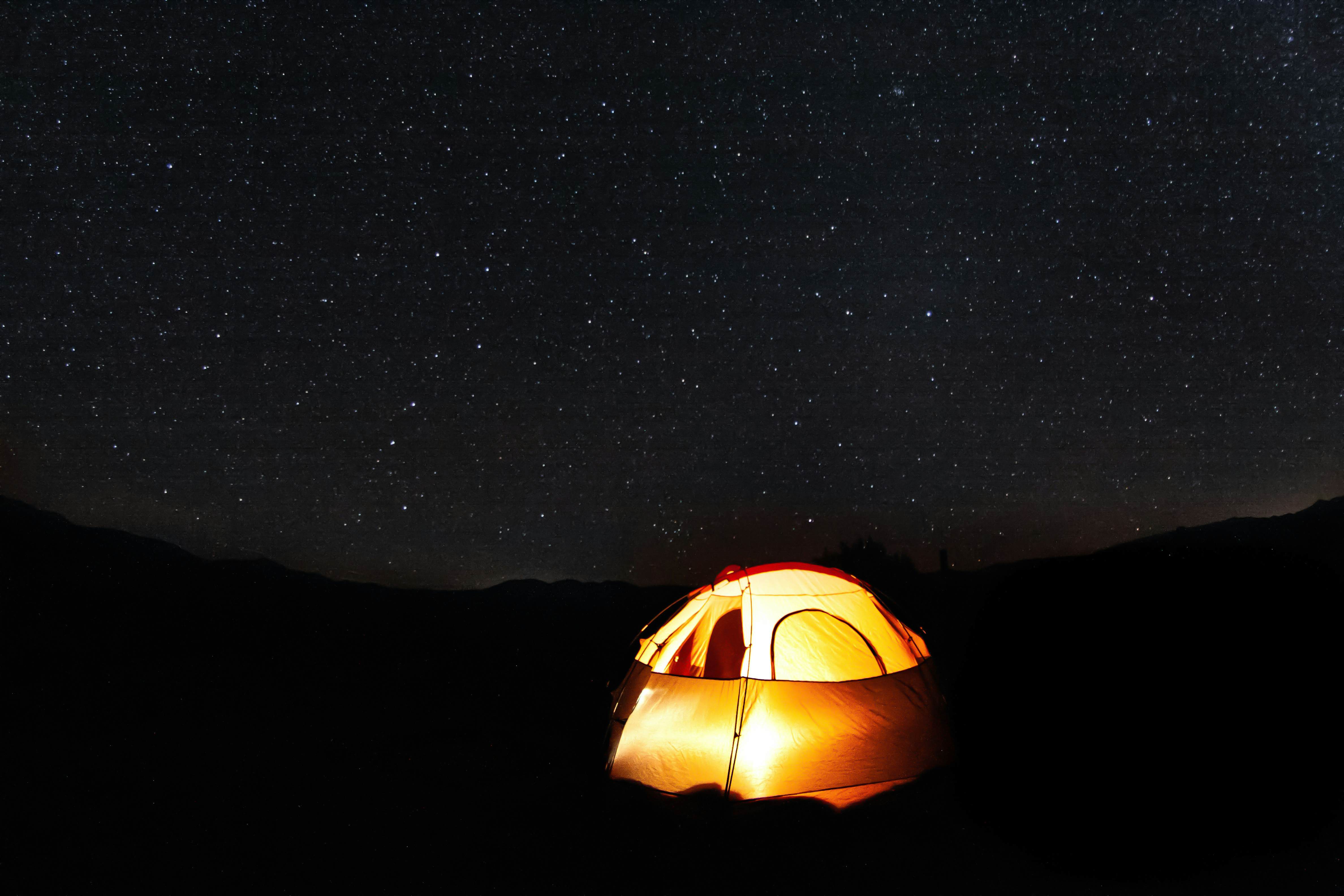 A tent is illuminated in orange light at a campground under a starry night sky