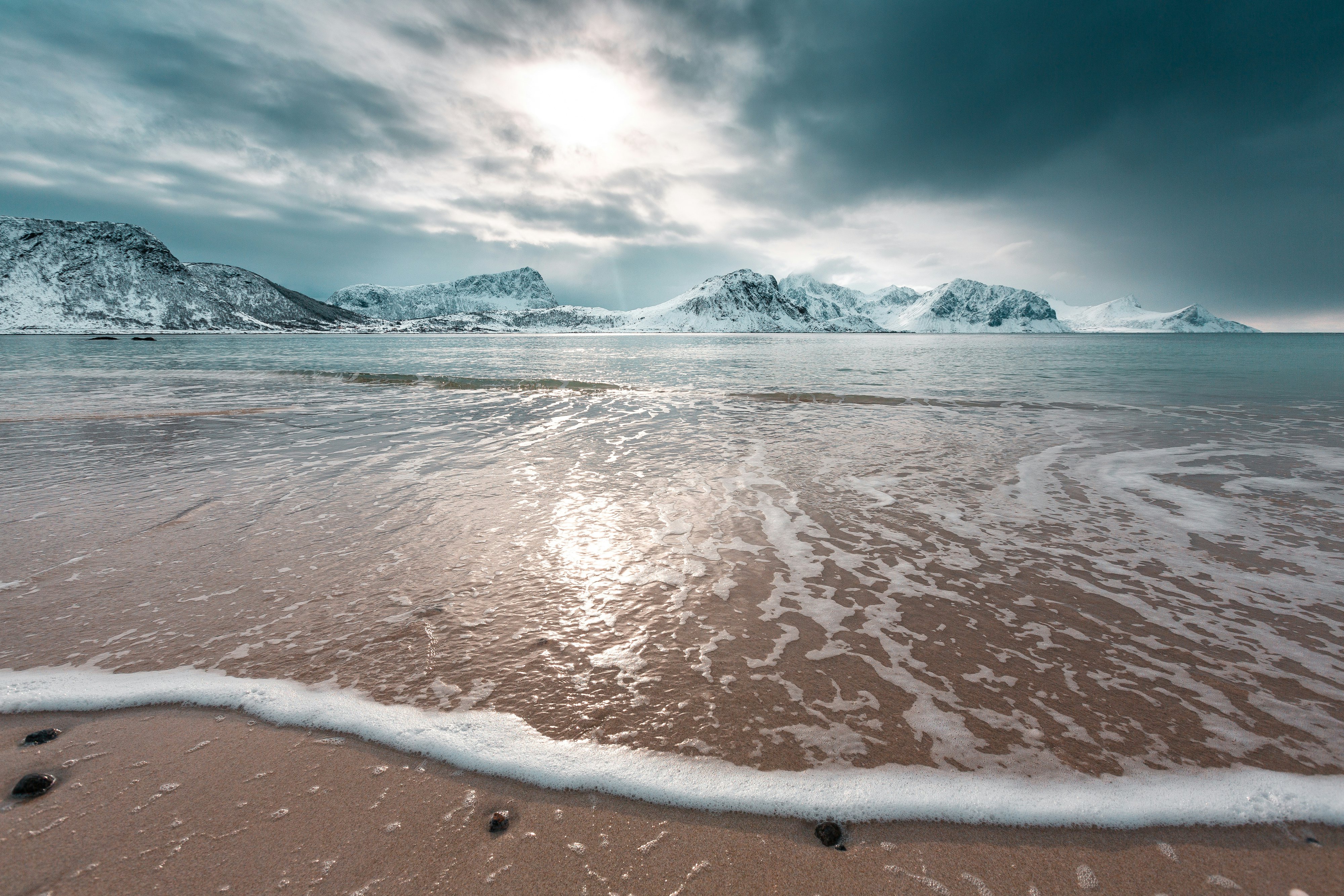 Haukland beach in winter with waves and snowcapped mountains in Lofoten, Norway.