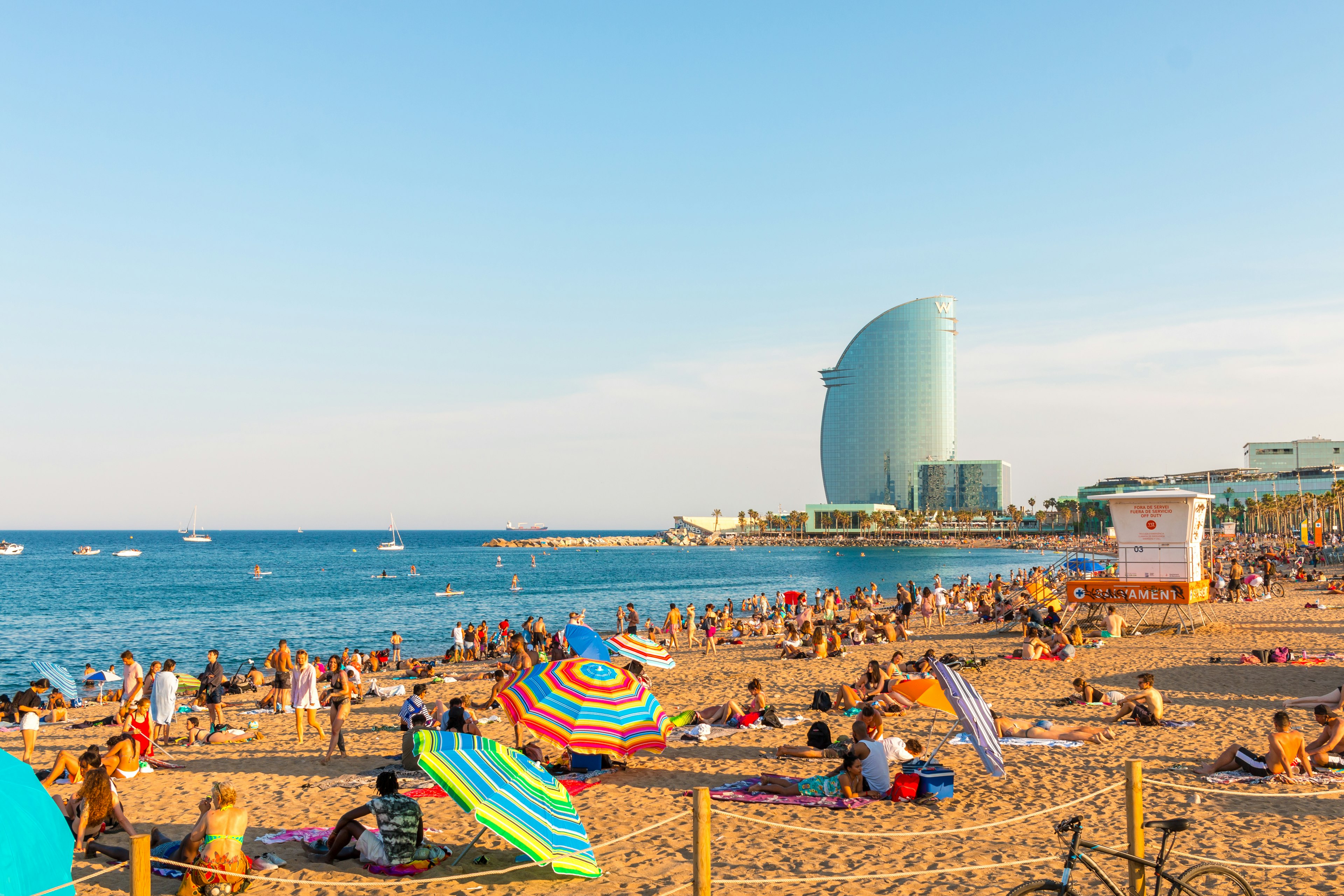 Colorful umbrellas dot a sandy beach overlooked by a tall curved glass building