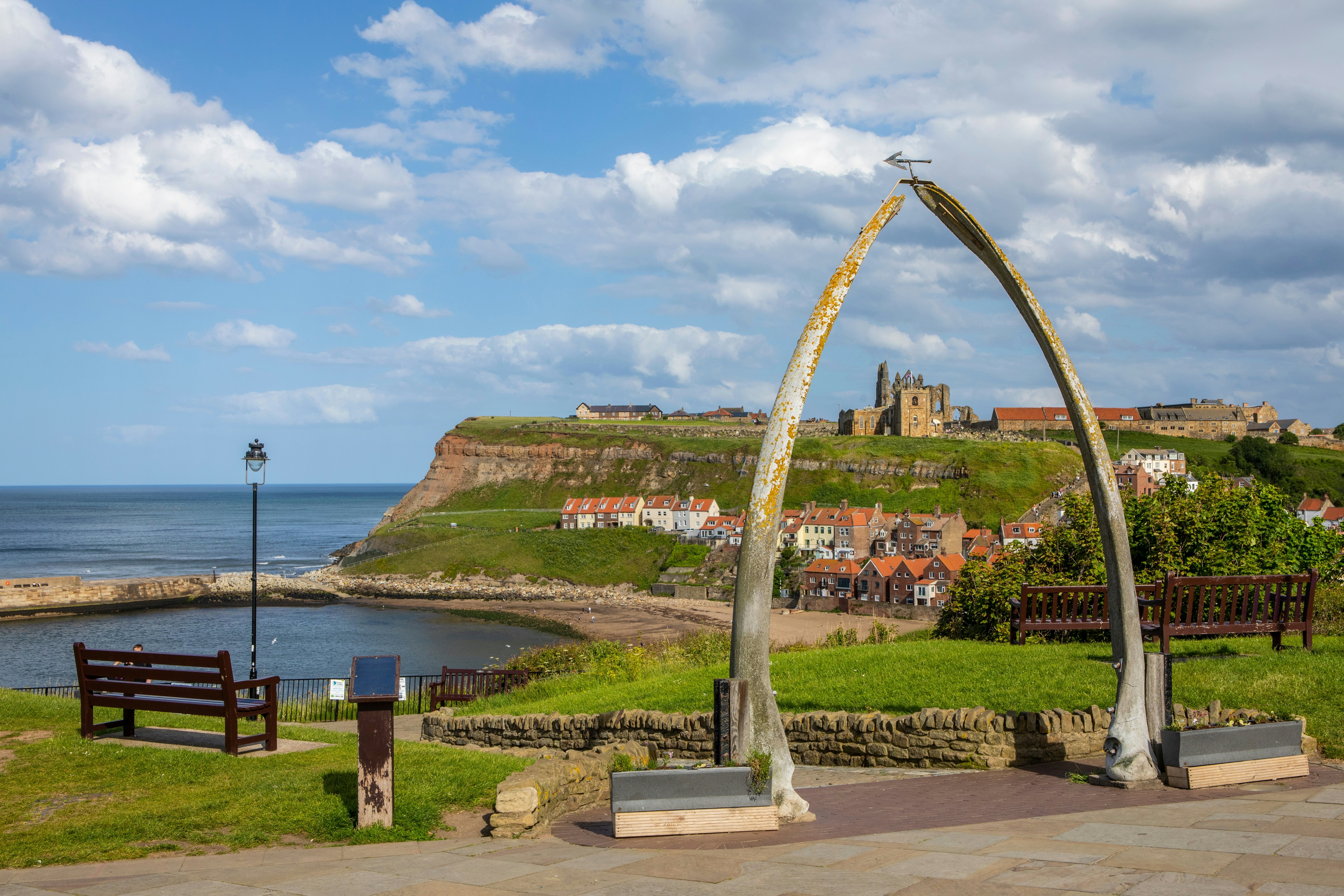 A large whale bone arch in a seaside town frames a church and ruined abbey on the distant cliff