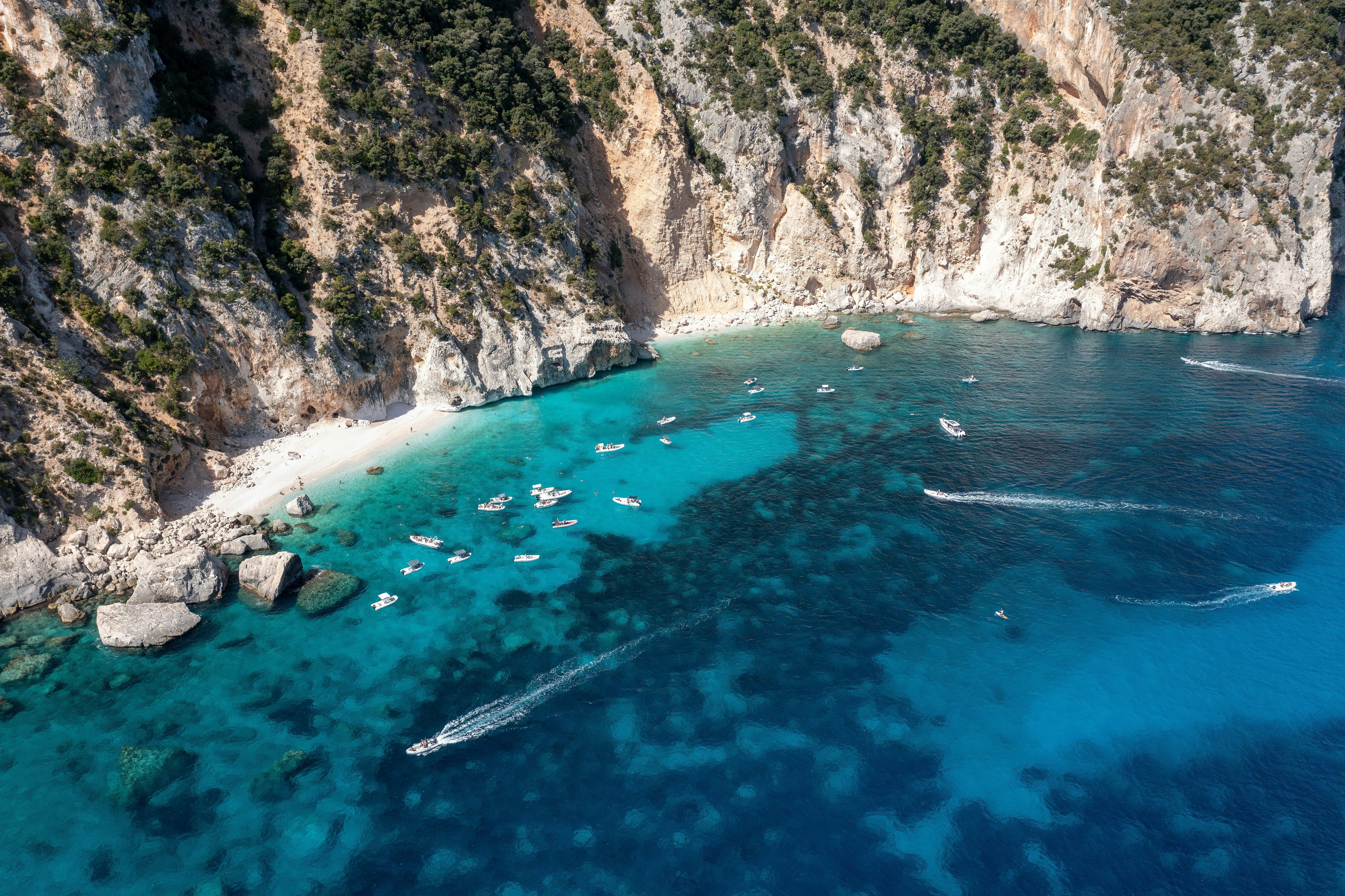 Aerial view of tourist boats along the rugged, cliff-lined coast of east Sardinia in the Golfo di Orosei near the quaint seaside town of Cala Gonone.