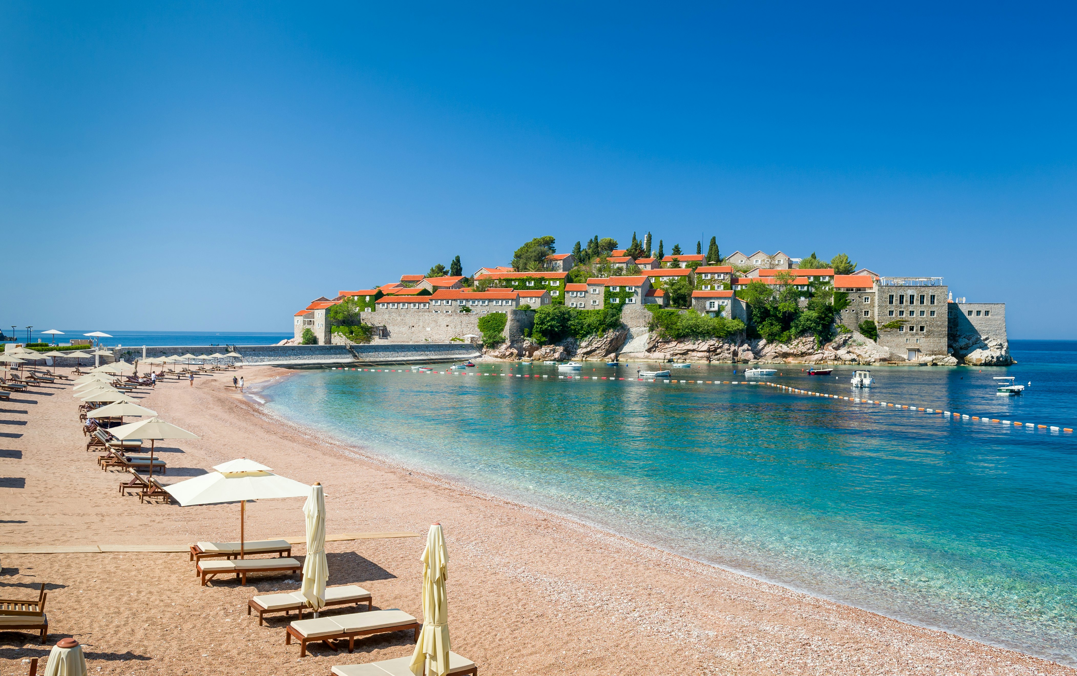 Luxury sand beach with wooden chaise-longue chairs and umbrellas near the Sveti Stefan historical town on the island of Montenegro.