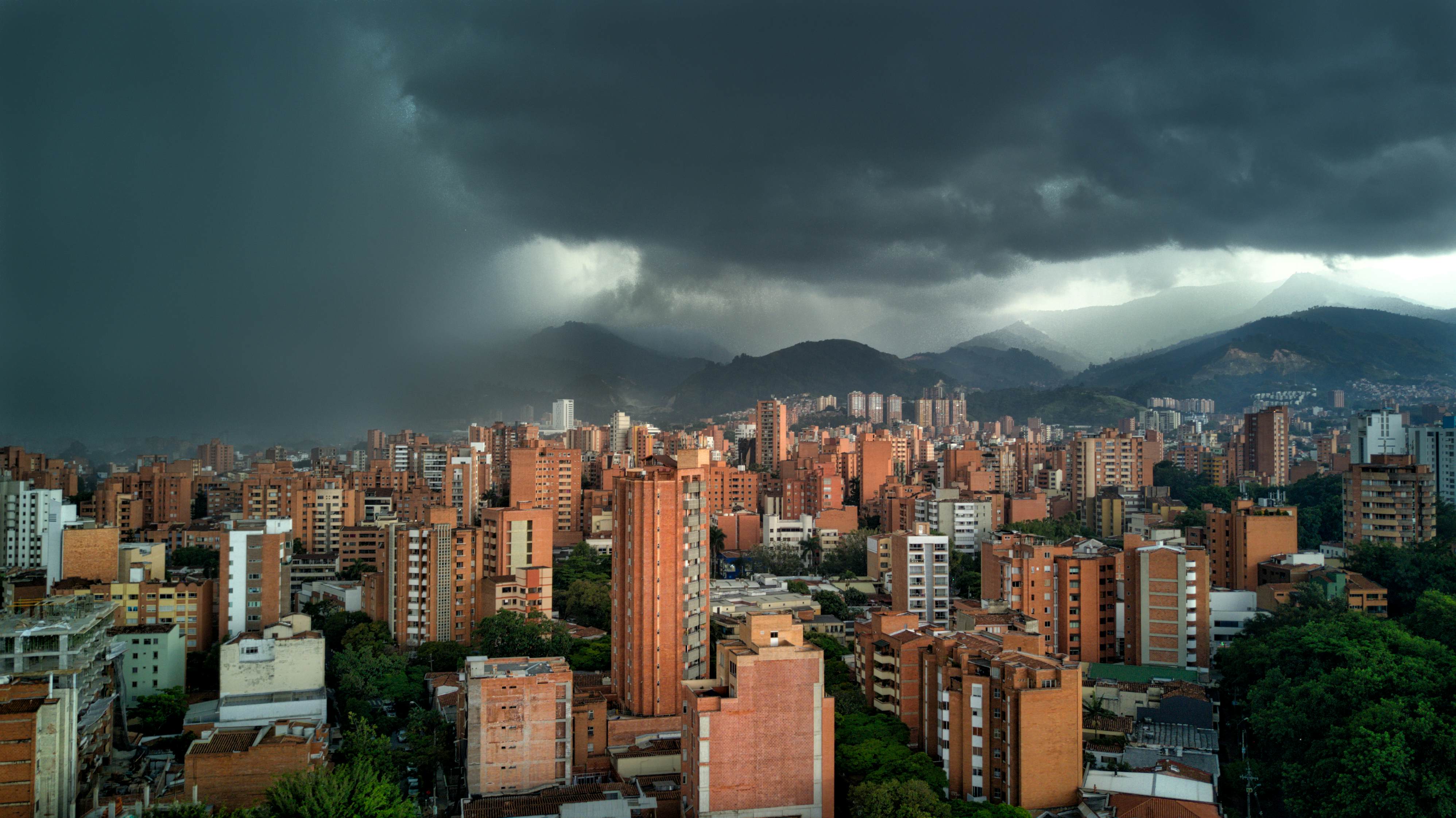 Dark storm clouds loom over towers in a city in a valley.